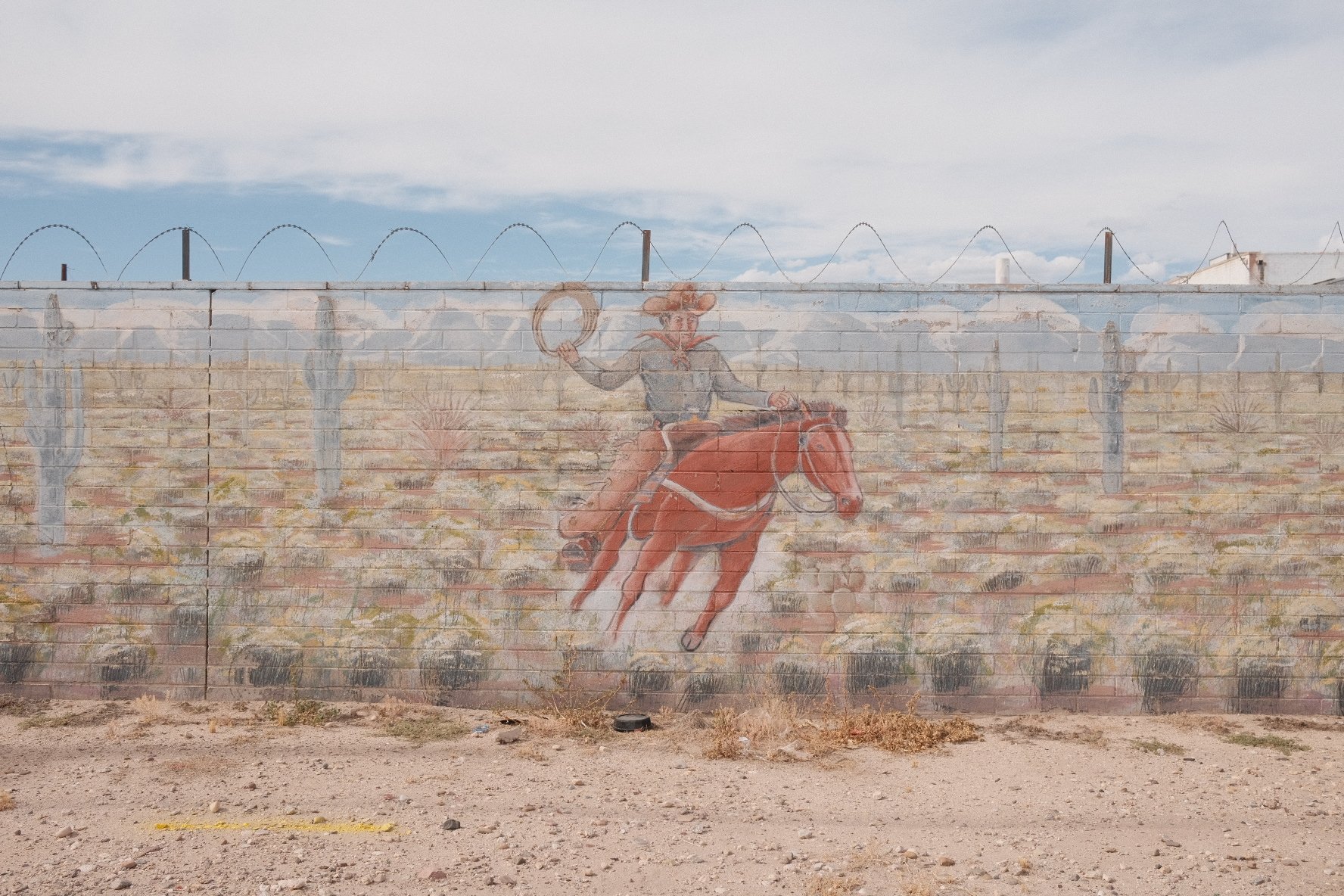A mural of a cowboy riding a bucking horse painted on a brick wall, with desert scenery and cacti in the background.