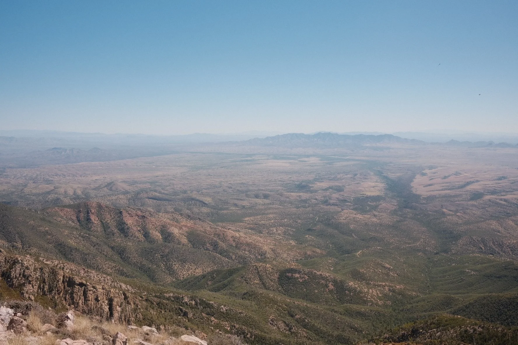 A vast desert landscape with mountain ranges in the distance under a clear blue sky.