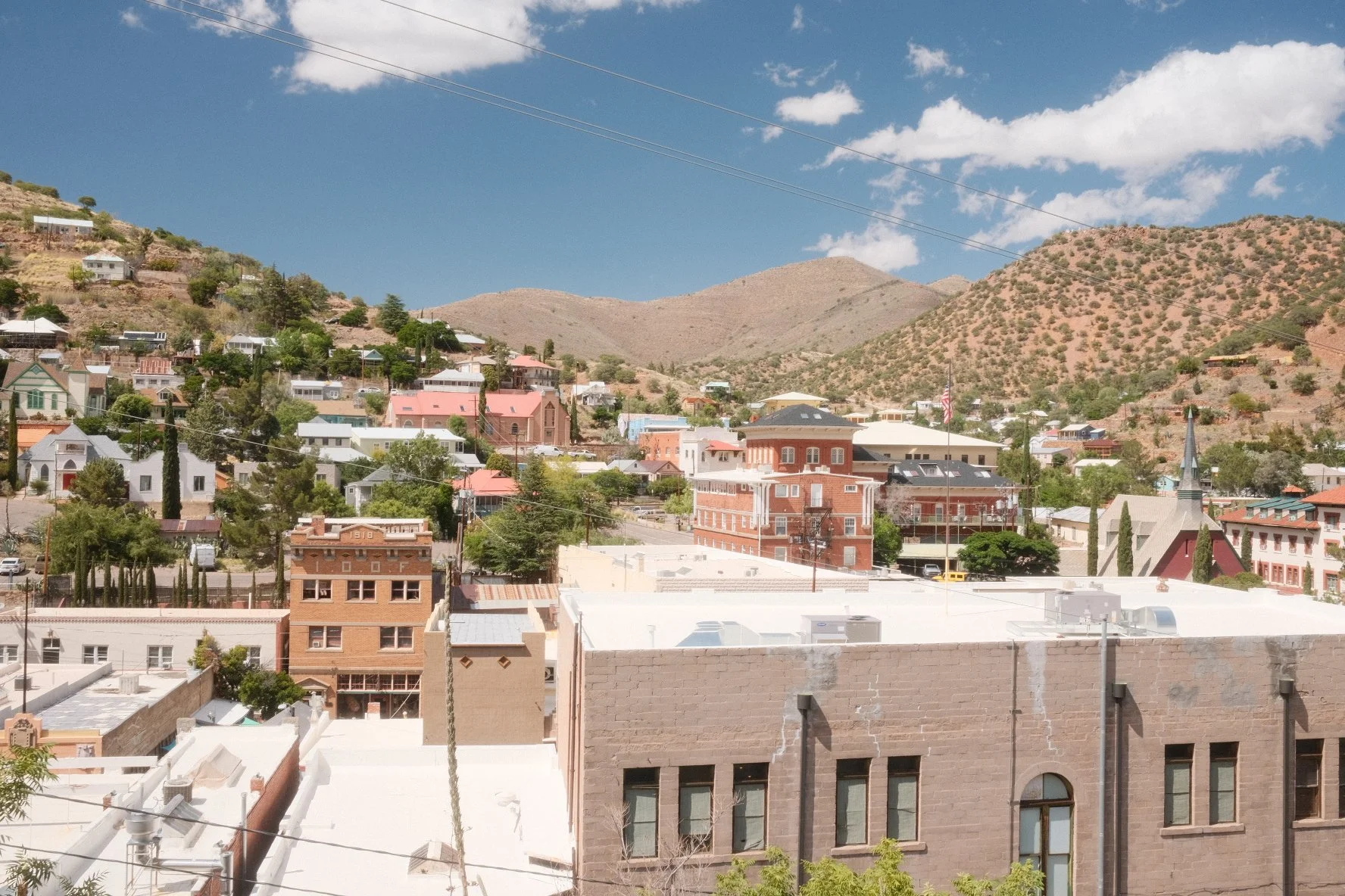 A view of a small town or city with colorful houses and buildings nestled in a hilly area with mountains in the background and a partly cloudy sky.