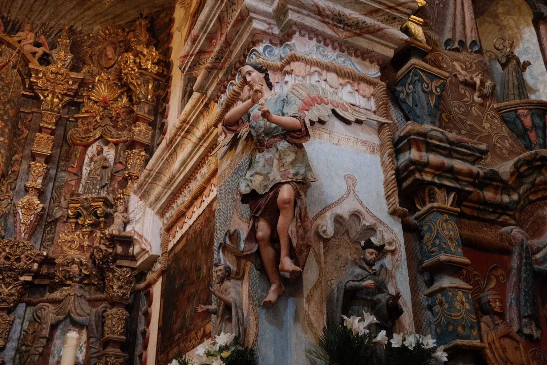 Church altar with a detailed religious sculpture of Jesus Christ with wings, surrounded by ornate gold and wood carvings, and smaller statues.