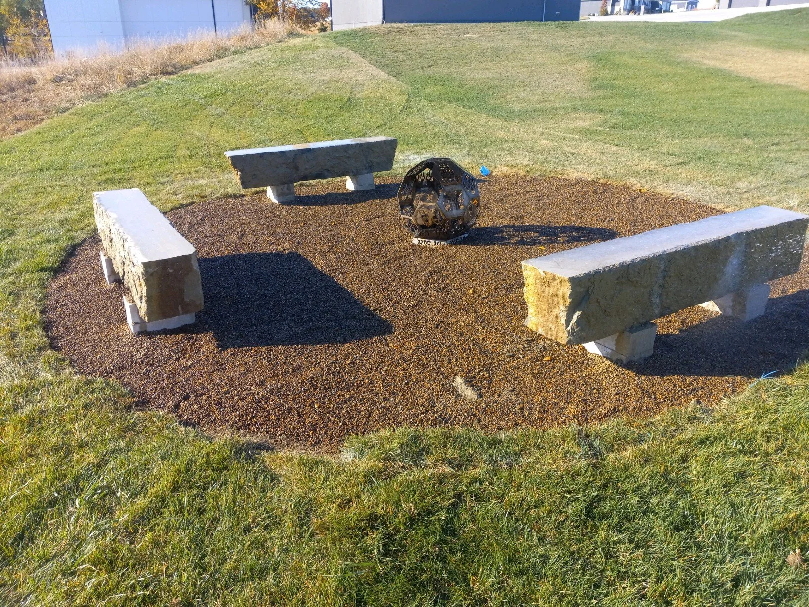 Outdoor stone benches surrounding a fire pit on a grassy lawn.