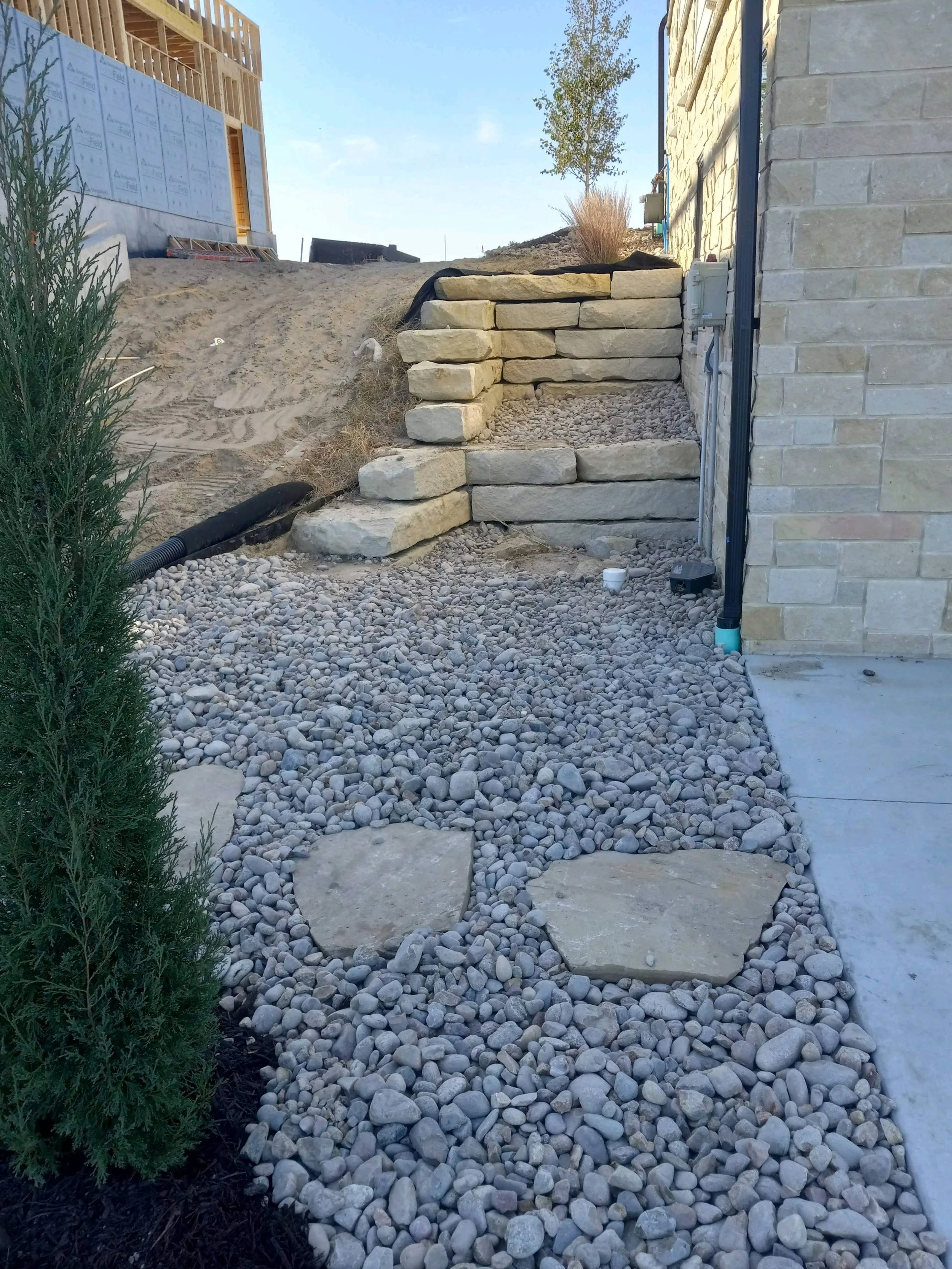 Stone steps leading up a small hill with surrounding gravel and a partially built house nearby.