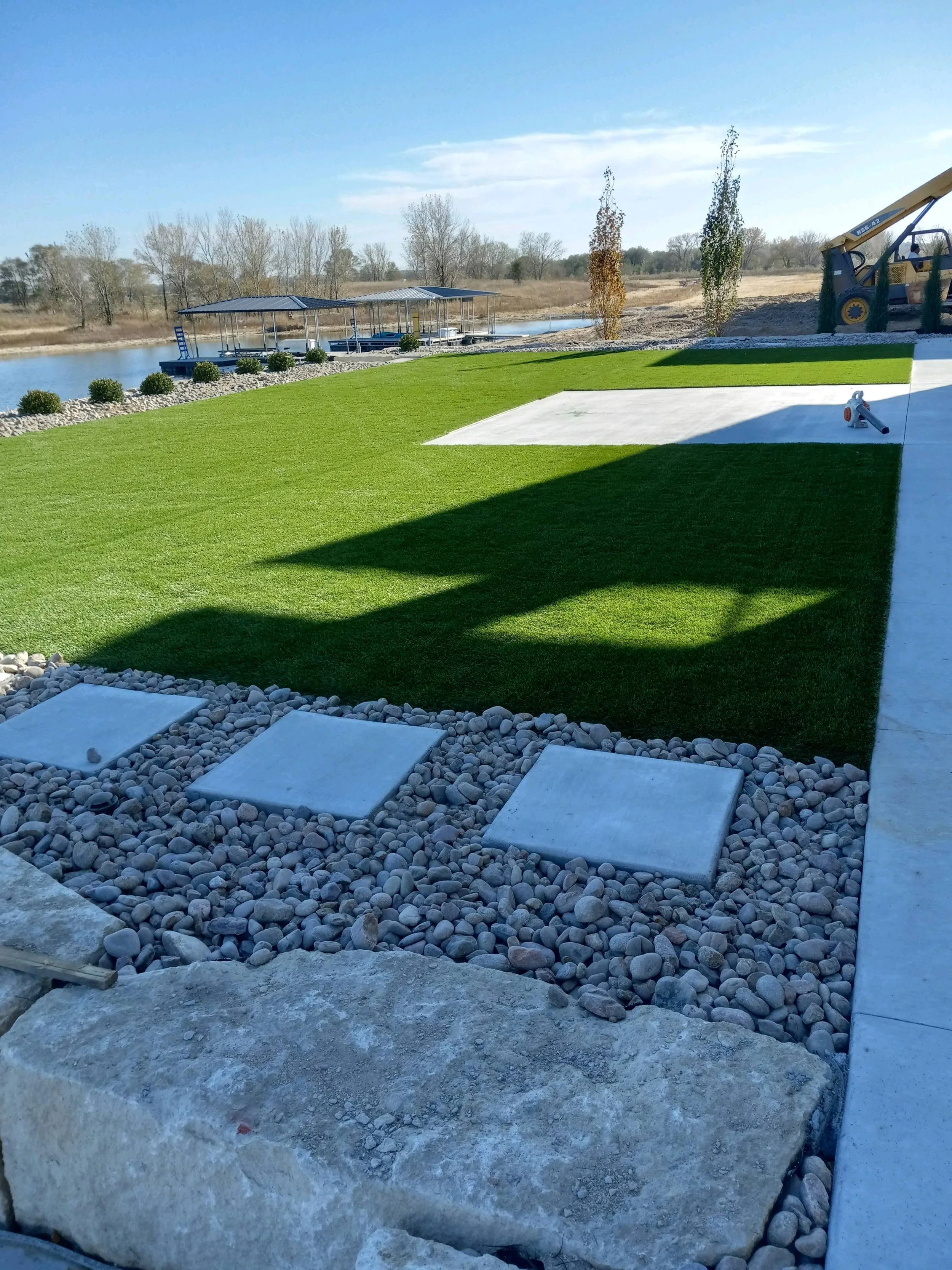 Landscape with a lawn, pathway, and dock at a lake; construction equipment visible.