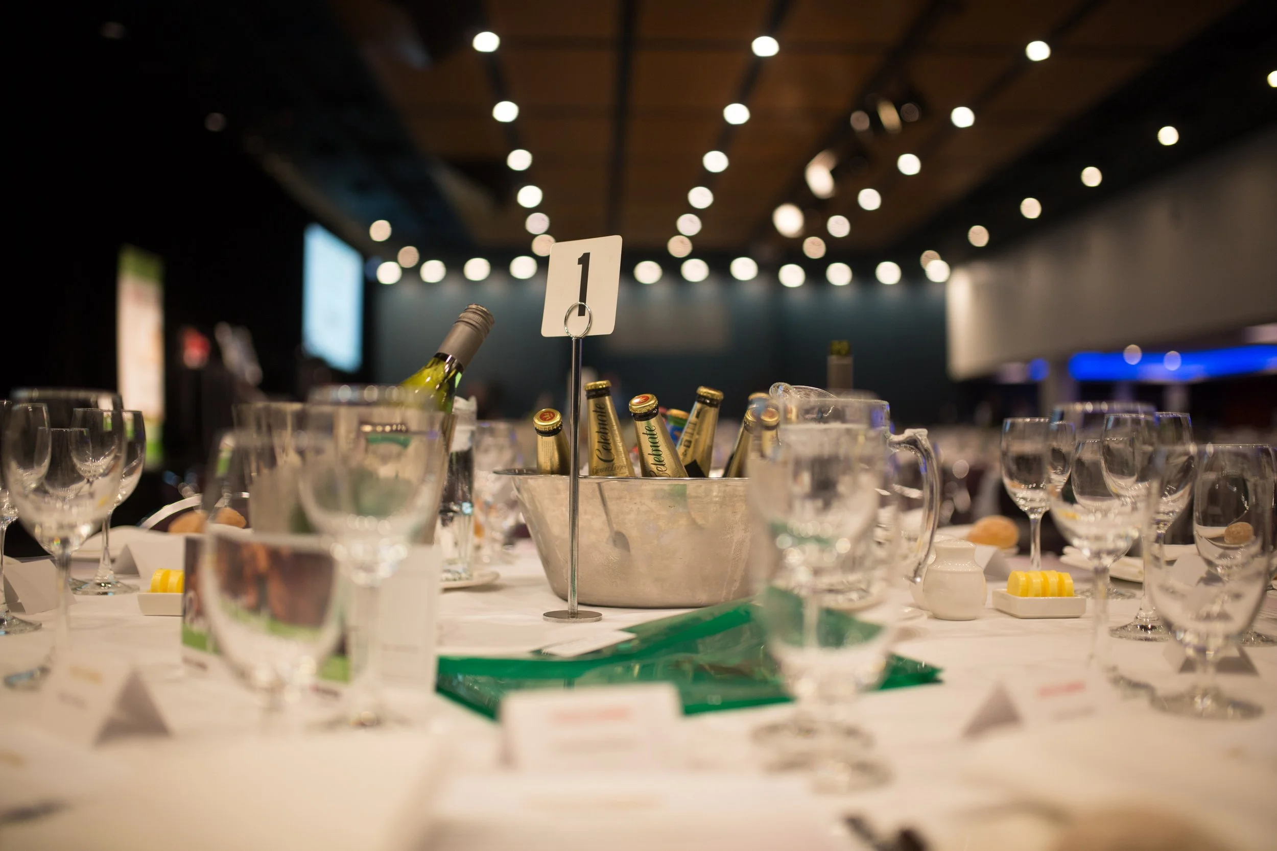 A conference room or banquet hall setup with tables, wine bottles in ice buckets, glasses, and place cards, ready for an event or meeting.