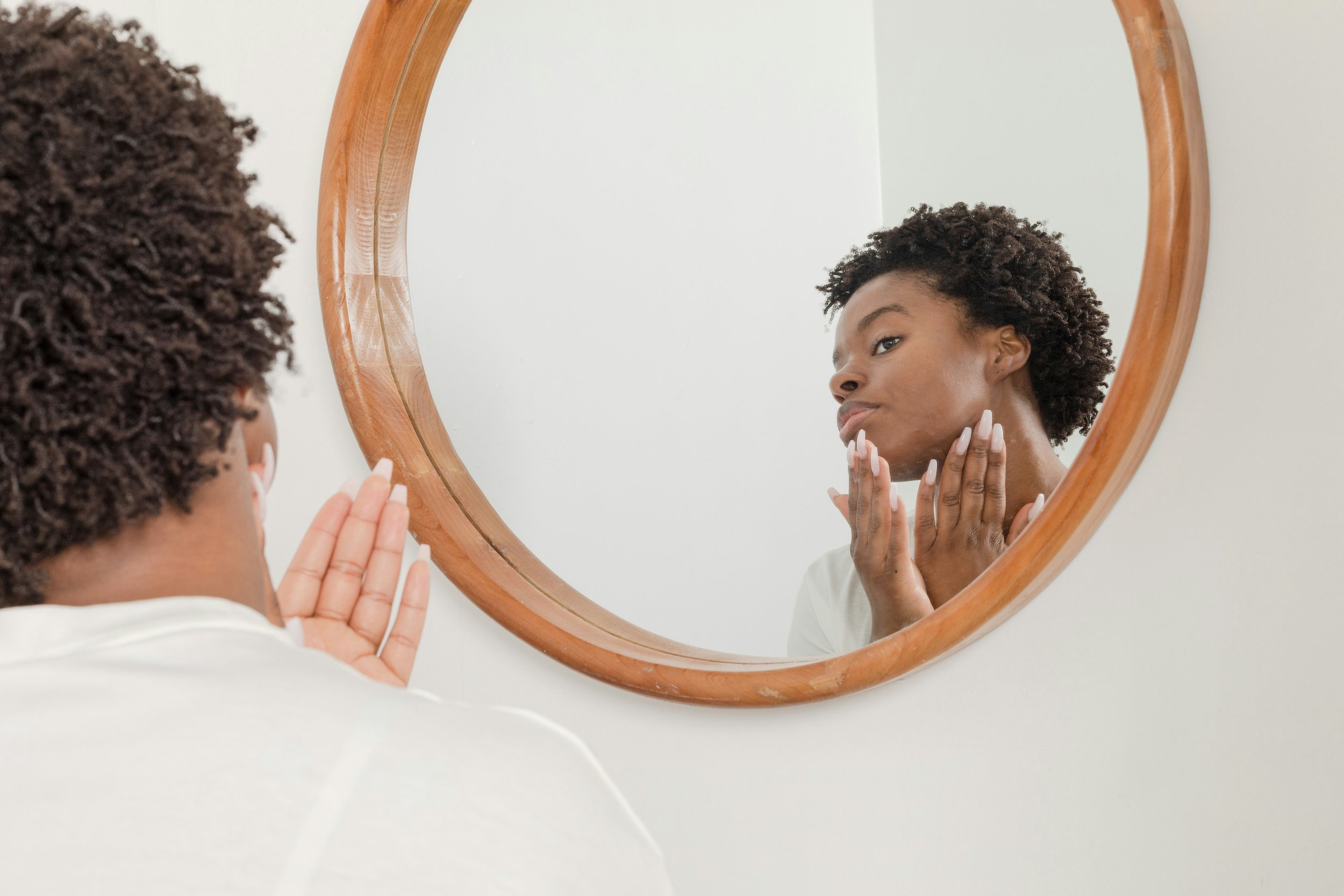 Black woman with natural hair looking at herself in the mirror and touching her face