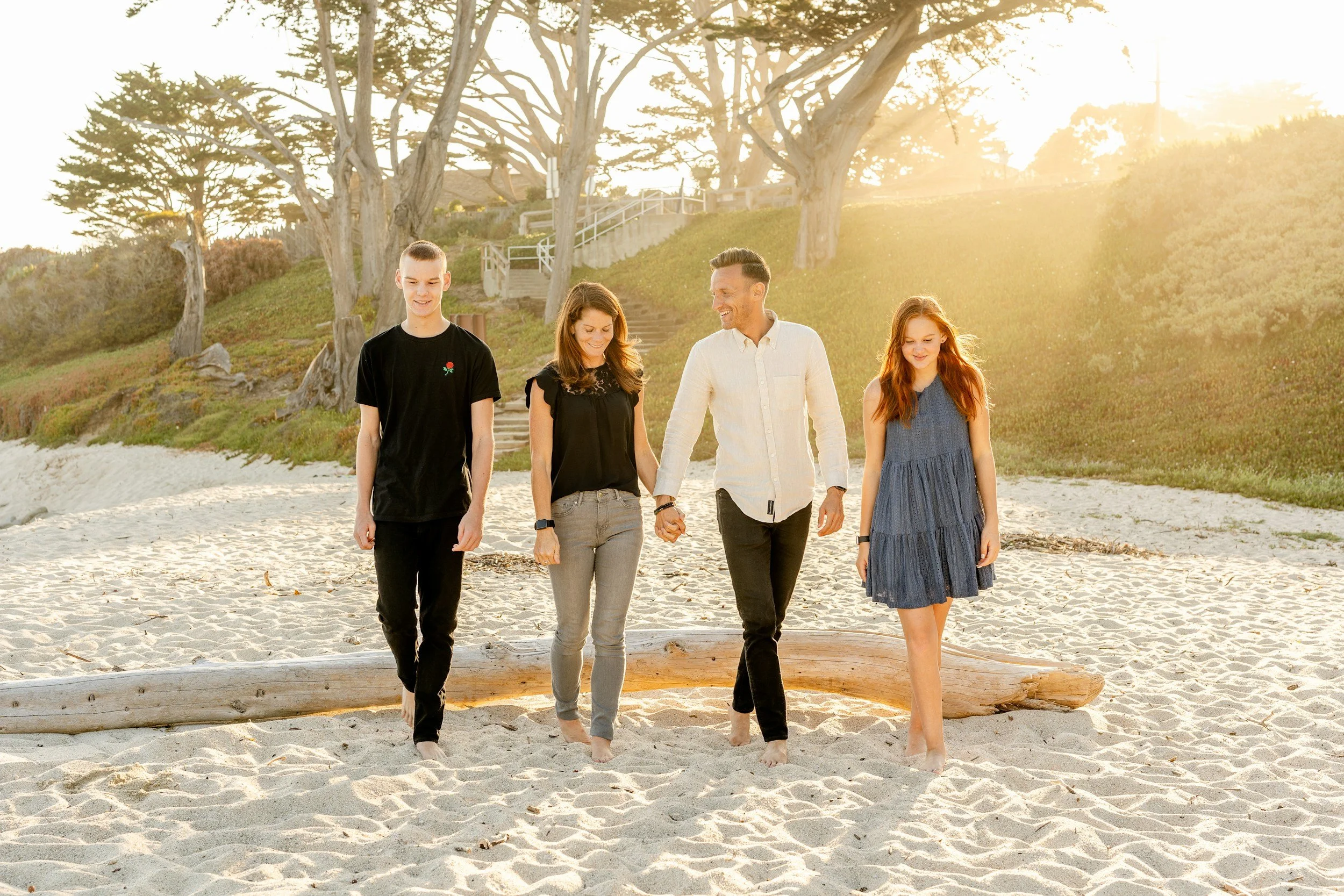 Family of four walking together on a sandy beach in the sunlight.