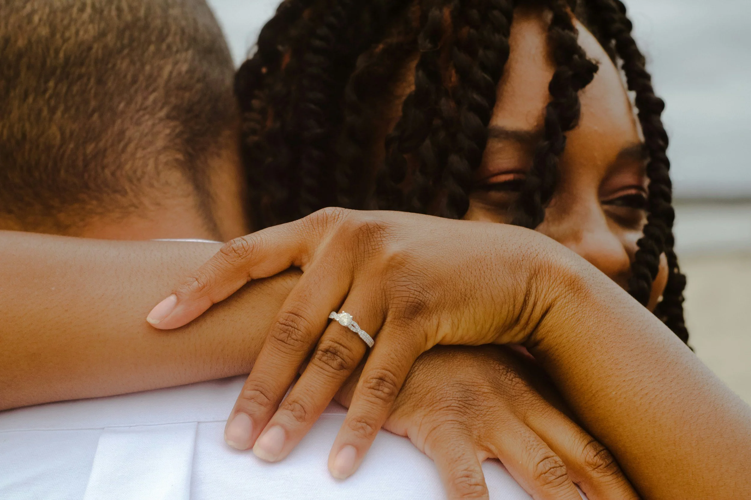 Close-up of a woman embracing her partner with an engagement ring visible on her hand.