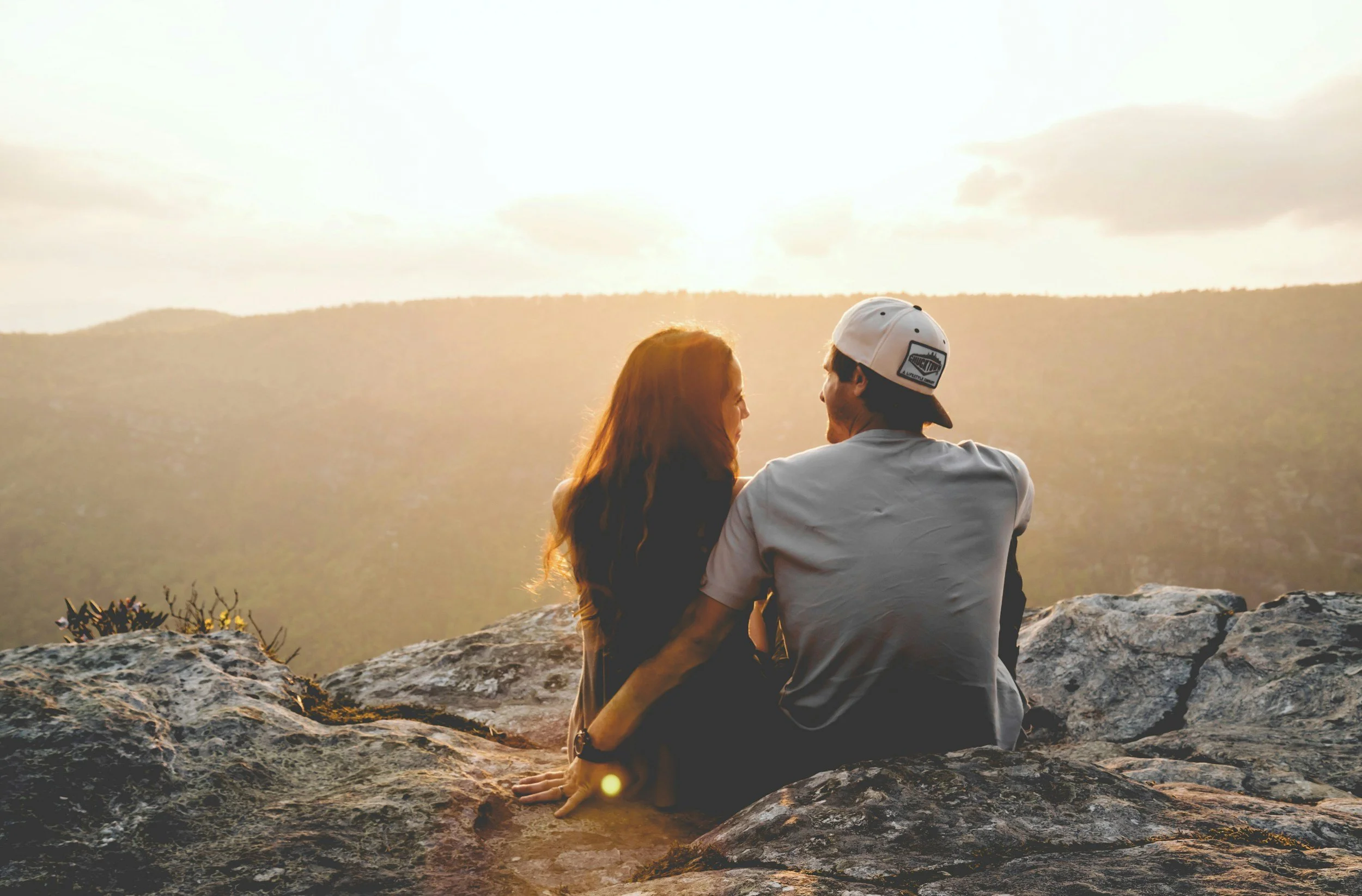 Couple sitting together on a rocky overlook at sunset with mountains in the distance.