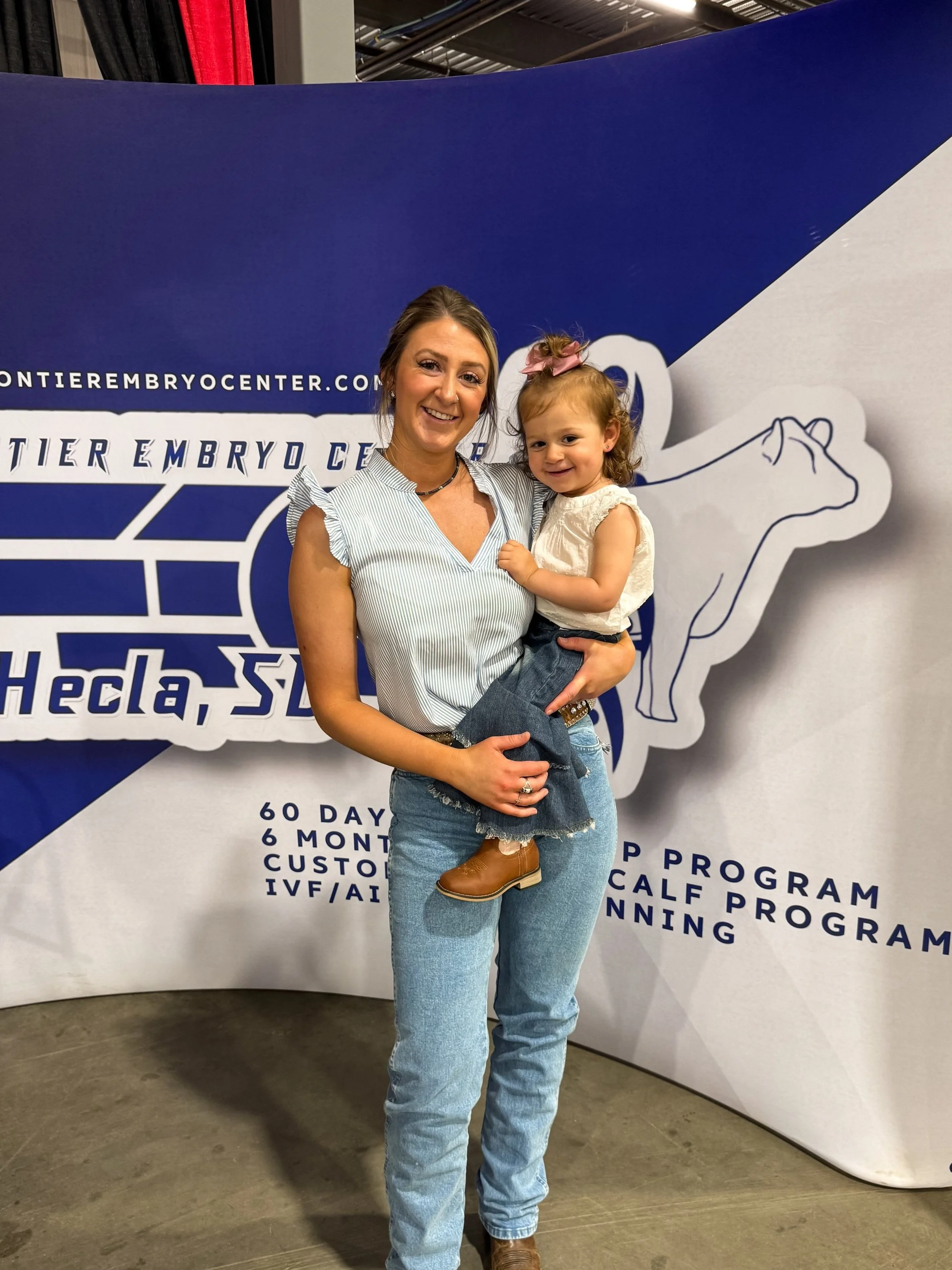 A family with a man, woman, and child standing outdoors in front of large metallic silos.