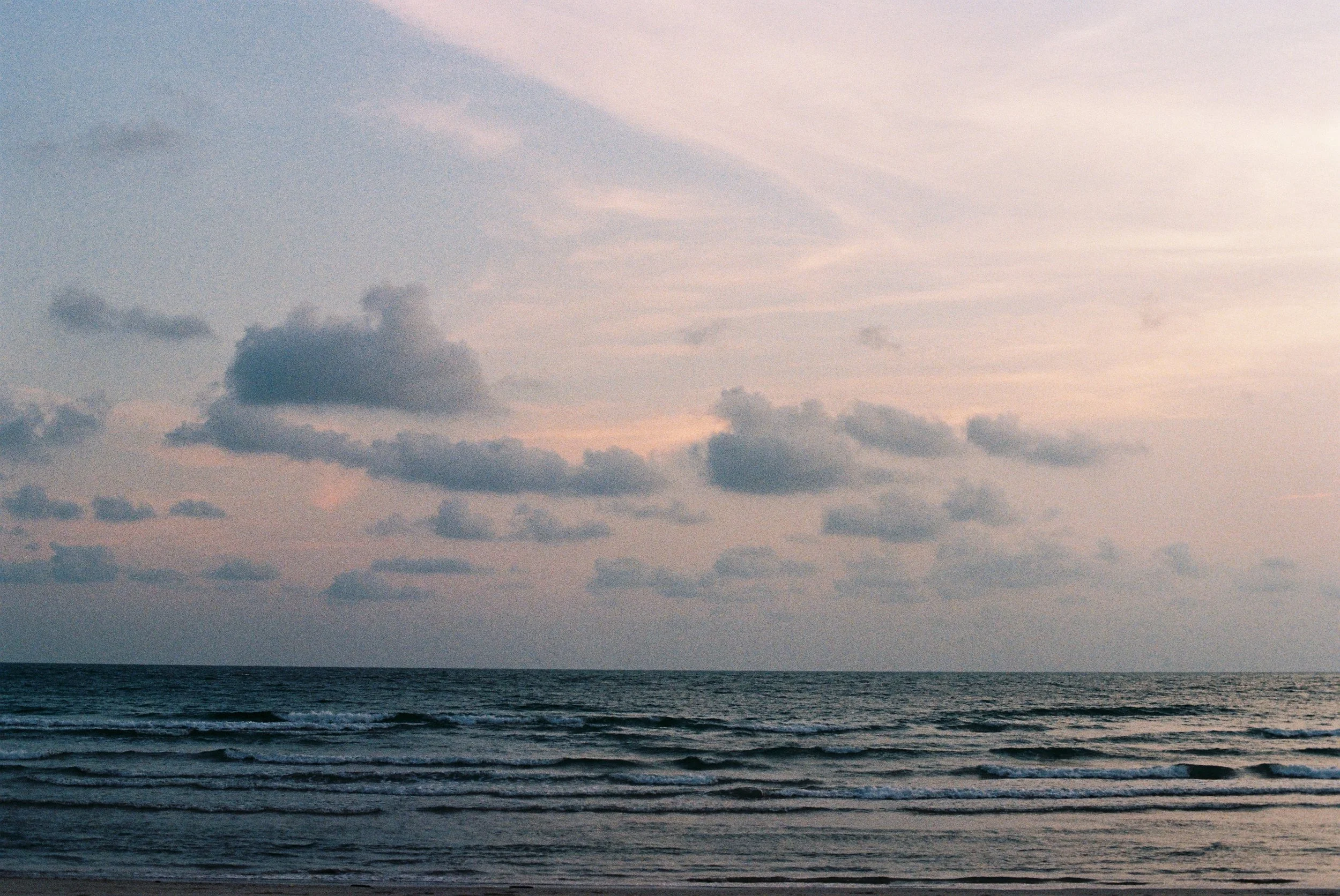 A view of the ocean with waves, under a sky filled with scattered clouds during dusk or dawn.