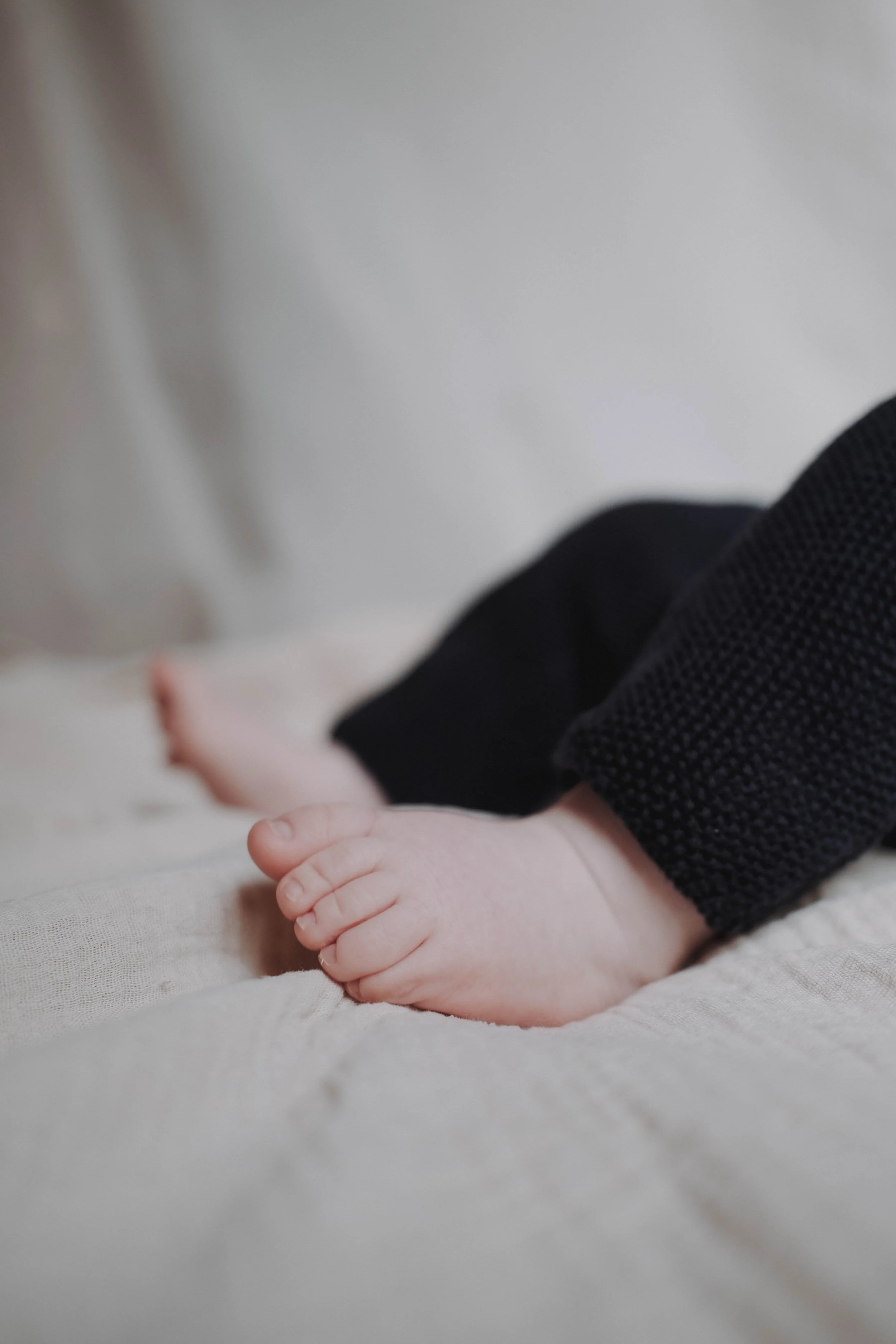 Nahaufnahme der winzigen Hand eines Babys mit schwarzen Kleidungsstücken, liegend auf einer weichen, hellen Oberfläche.