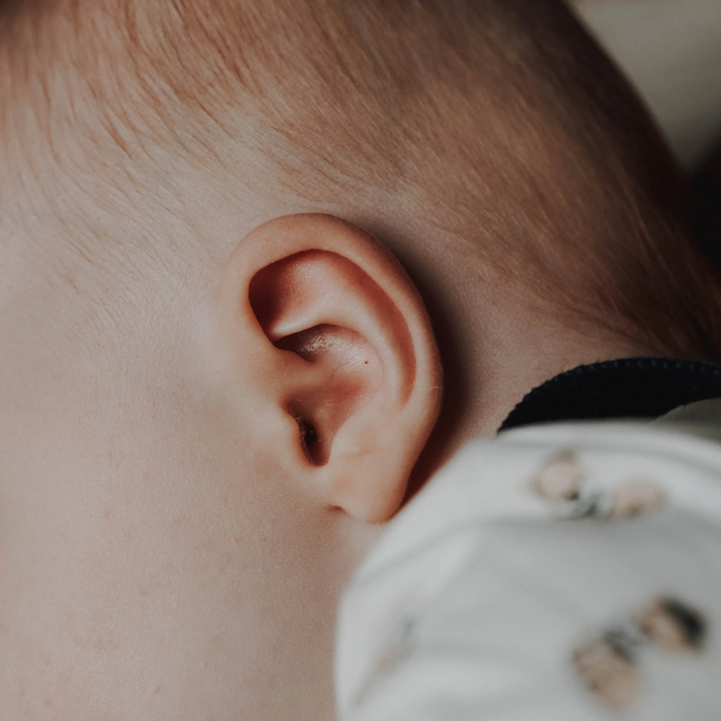 Nahaufnahme eines kindlichen Ohrs mit braunen Haaren im Hintergrund.