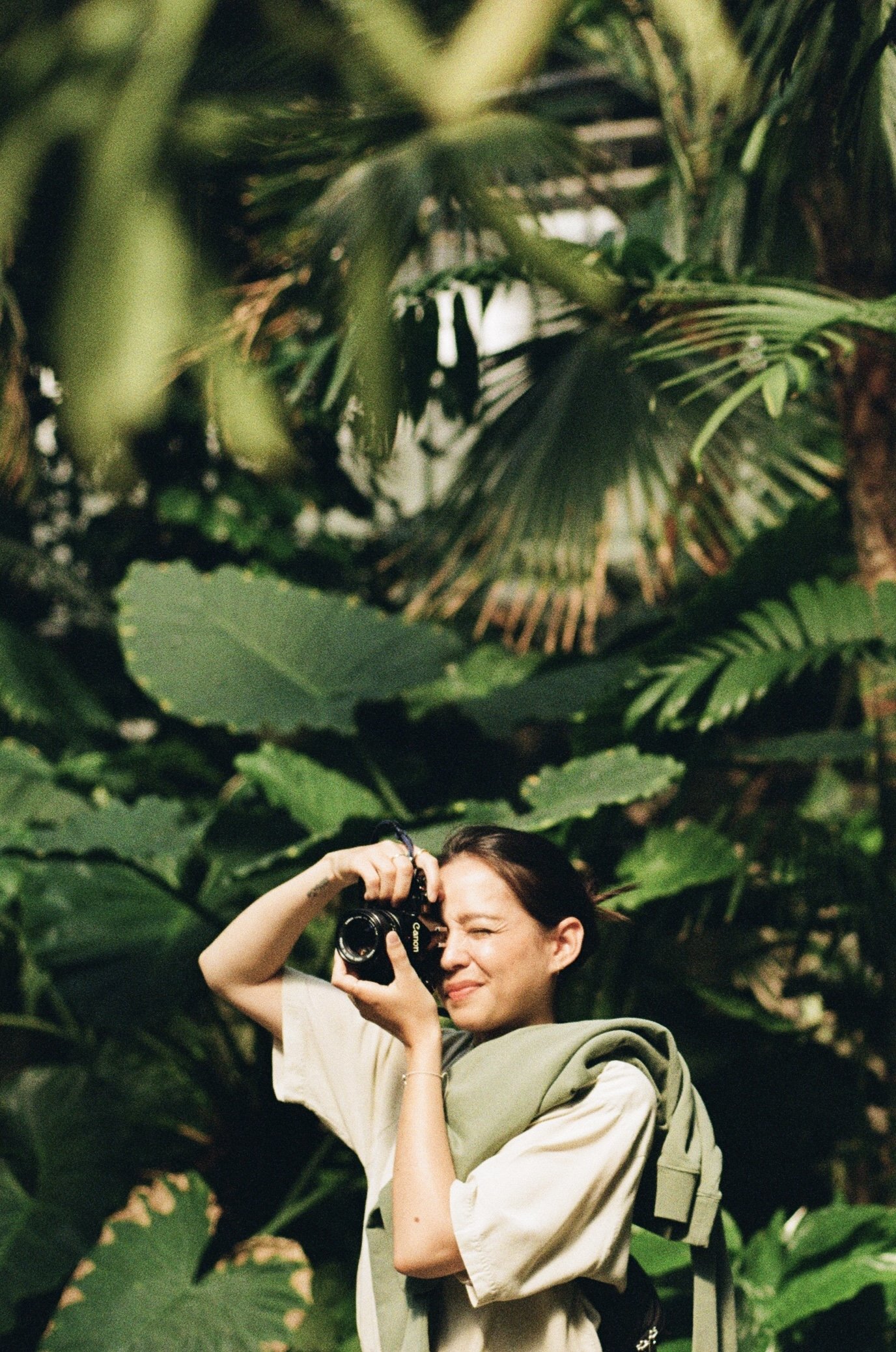 Junge Frau in einer grünen Dschungellandschaft macht Fotos mit einer Kamera.