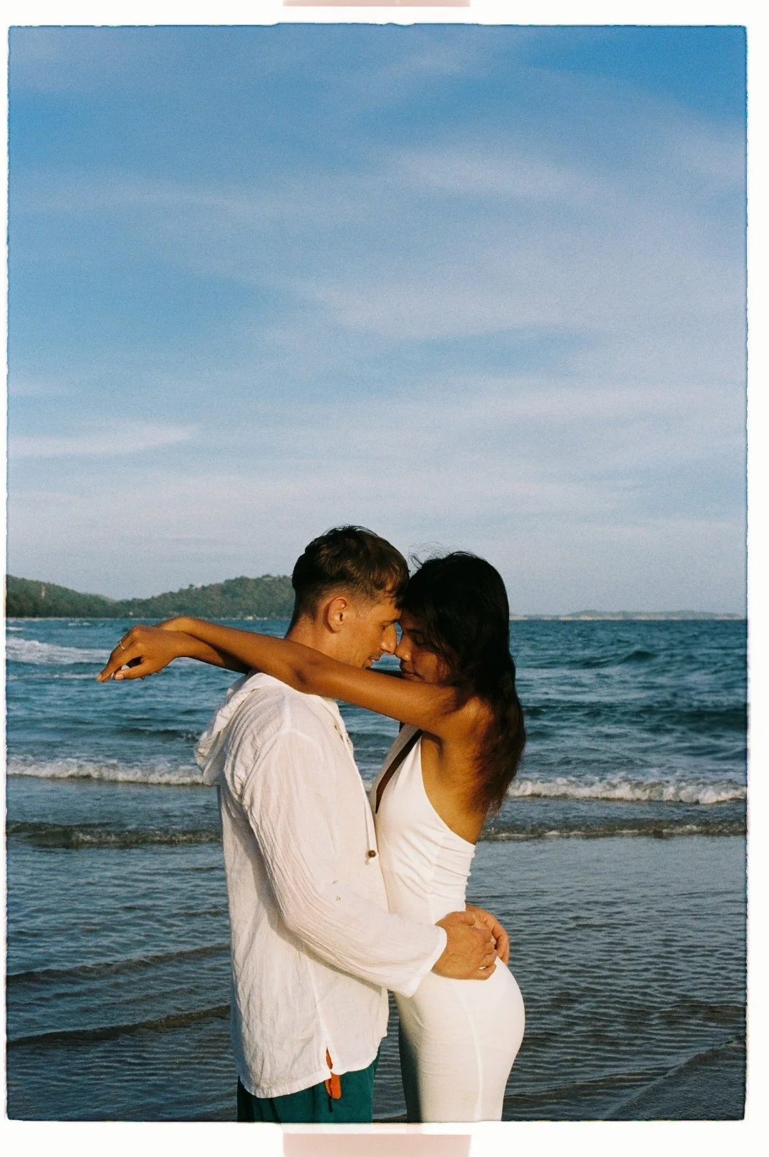 A couple embracing on the beach with the ocean in the background.