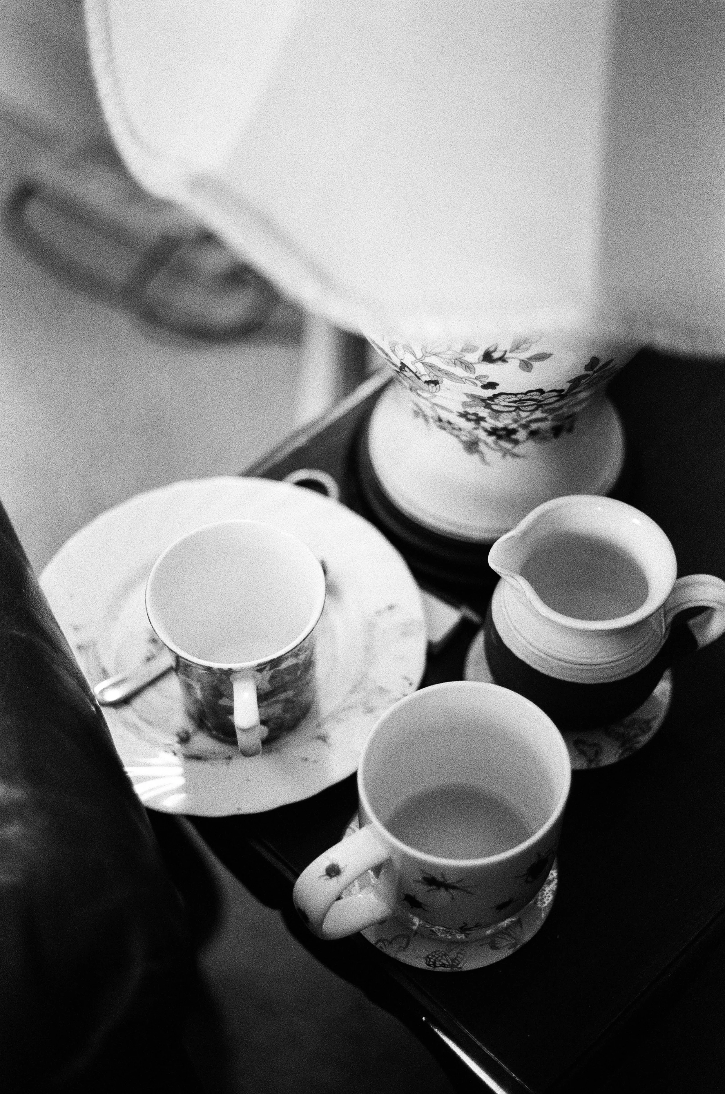 Black and white photo of a kitchen countertop with floral patterned mugs on a tray, a teapot, and a sugar bowl.