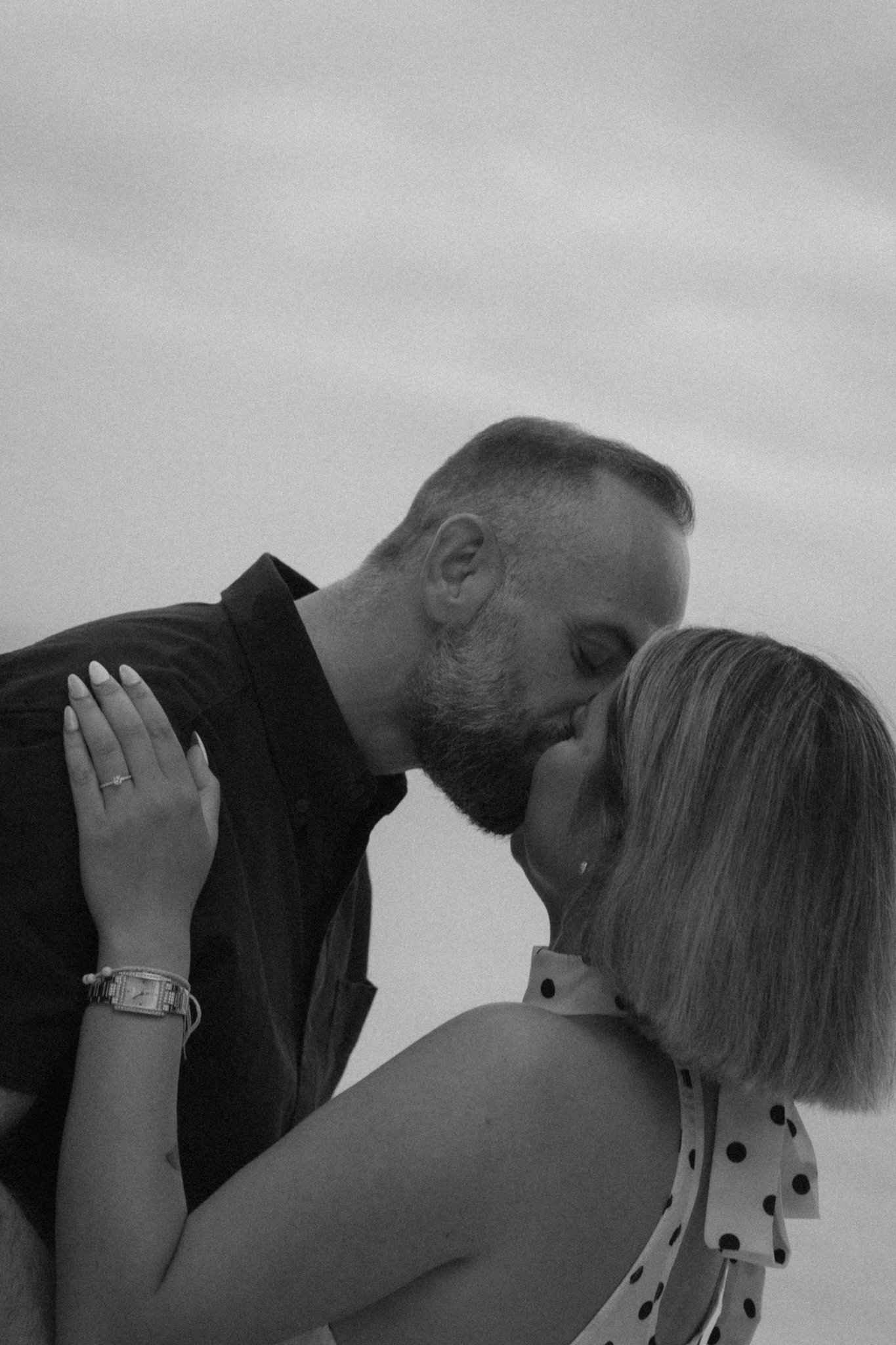 A man and woman in a close, intimate moment, possibly a kiss or about to kiss, with the man shirtless and the woman wearing a polka-dot dress, showing affection.