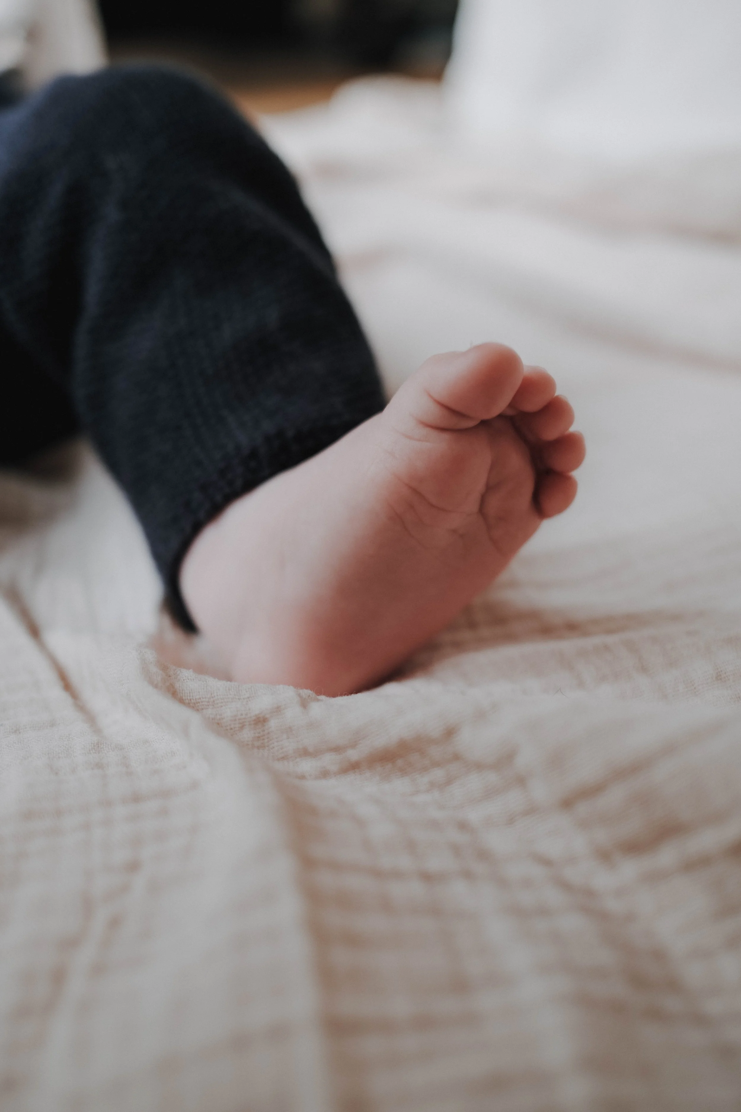 Nahaufnahme eines Babyhand, die auf einer weichen, hellfarbenen Decke liegt, mit einem dunklen langärmeligen Kleid.