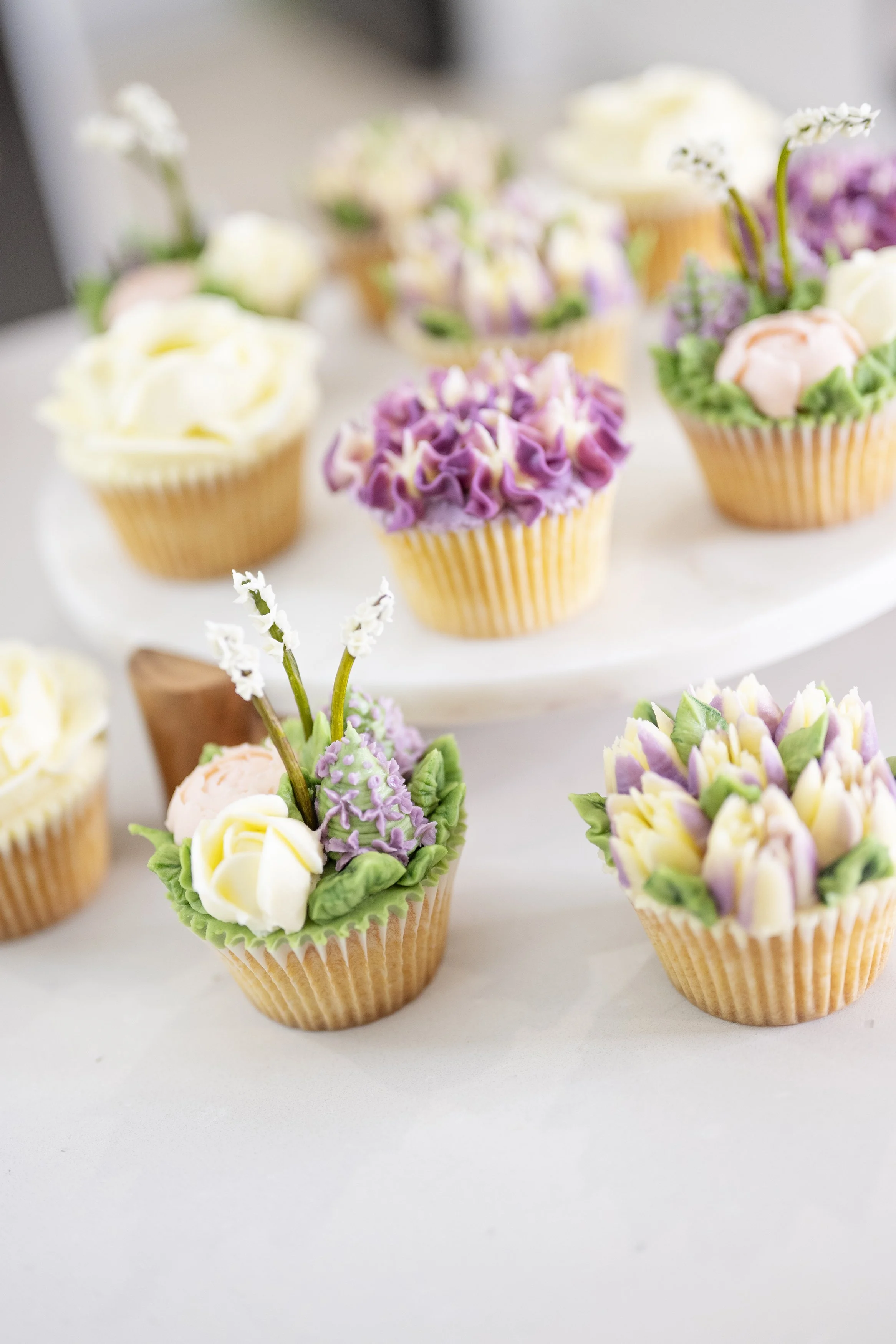 Decorative cupcakes with floral frosting and sugar flowers in pastel colors on a white cake stand.