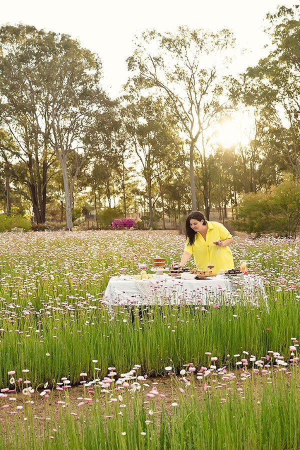 Photograher Mel at a table of treats in a field of flowers