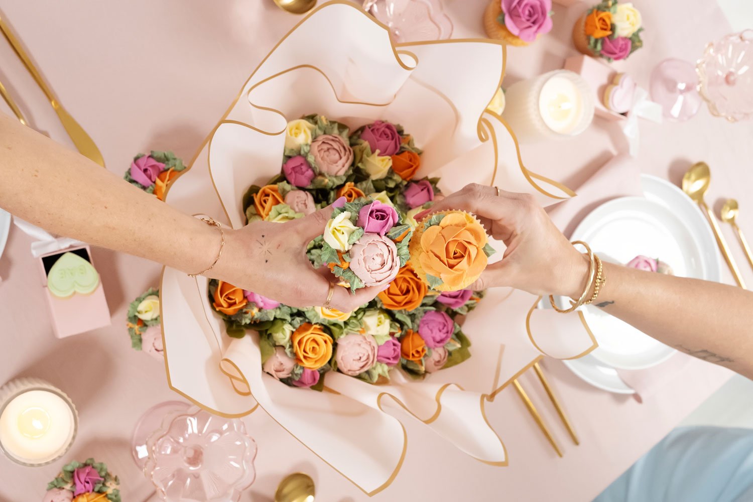 Two hands holding buttercream flower cupcakes over a larger cupcake bouquet