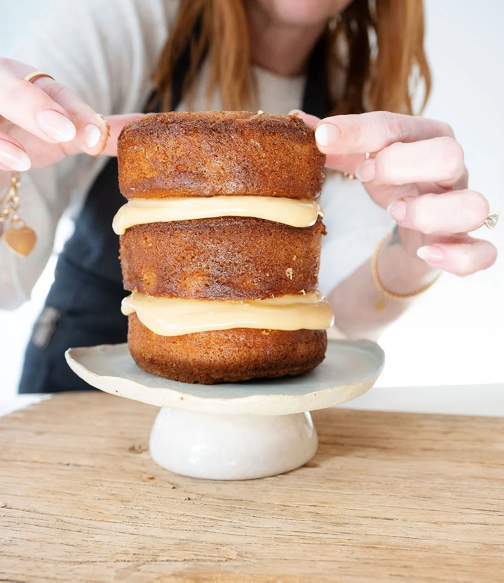 Woman's hands placing the third layer of a cake on a cake stand