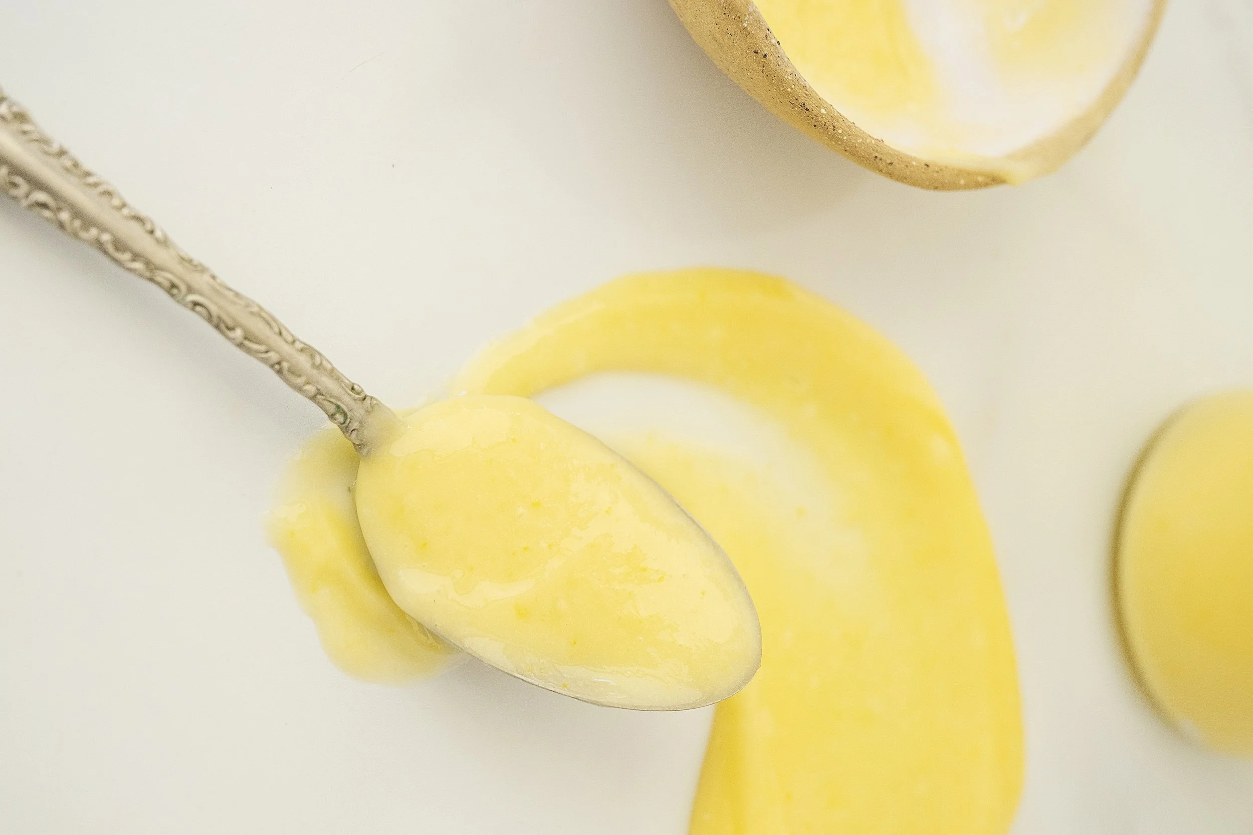 Lemon curd on a vintage spoon smeared on a white surface