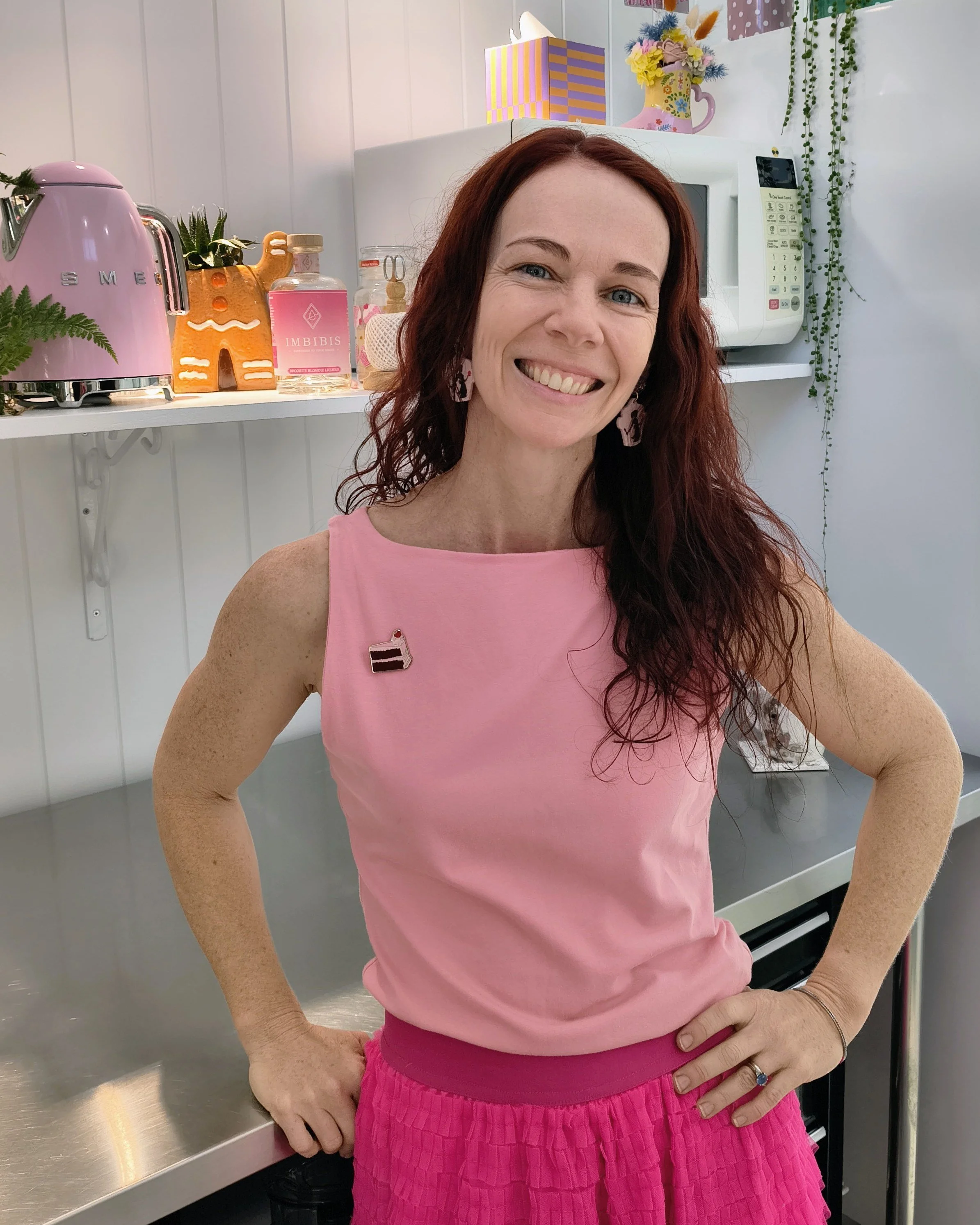 Brooke Arnolda of Baked by Brooke smiling in her pink studio kitchen