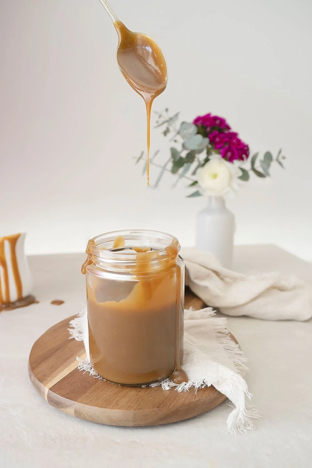 Caramel sauce in a jar being dripped from a spoon