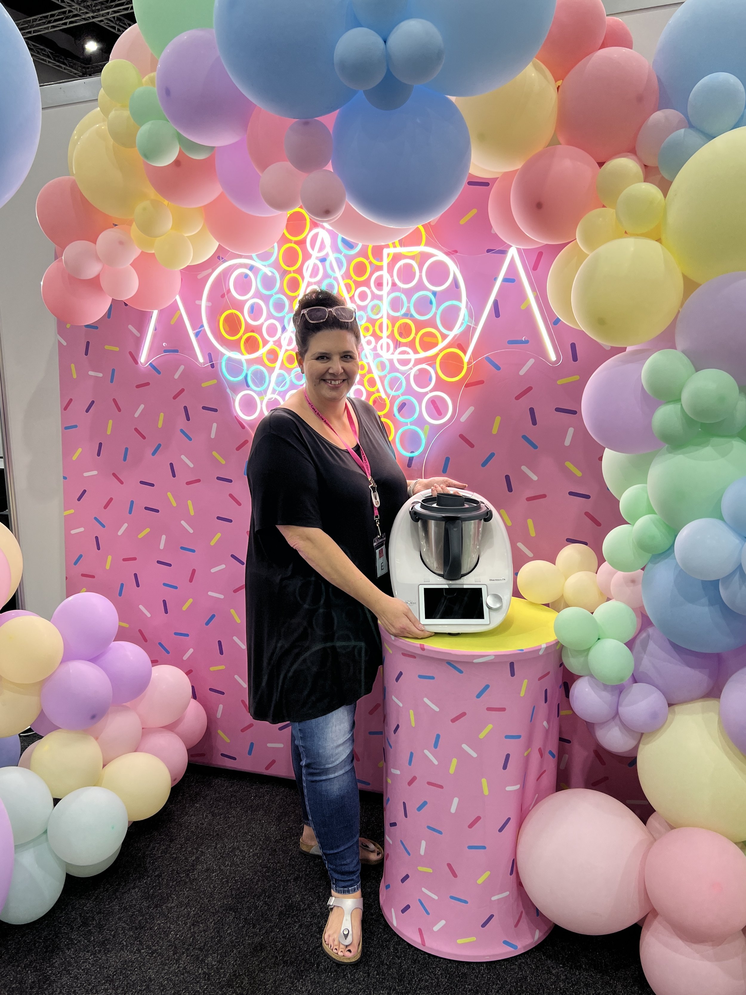 Mel stands next to a white thermomix in front of an ACADA sprinkle baloon backdrop