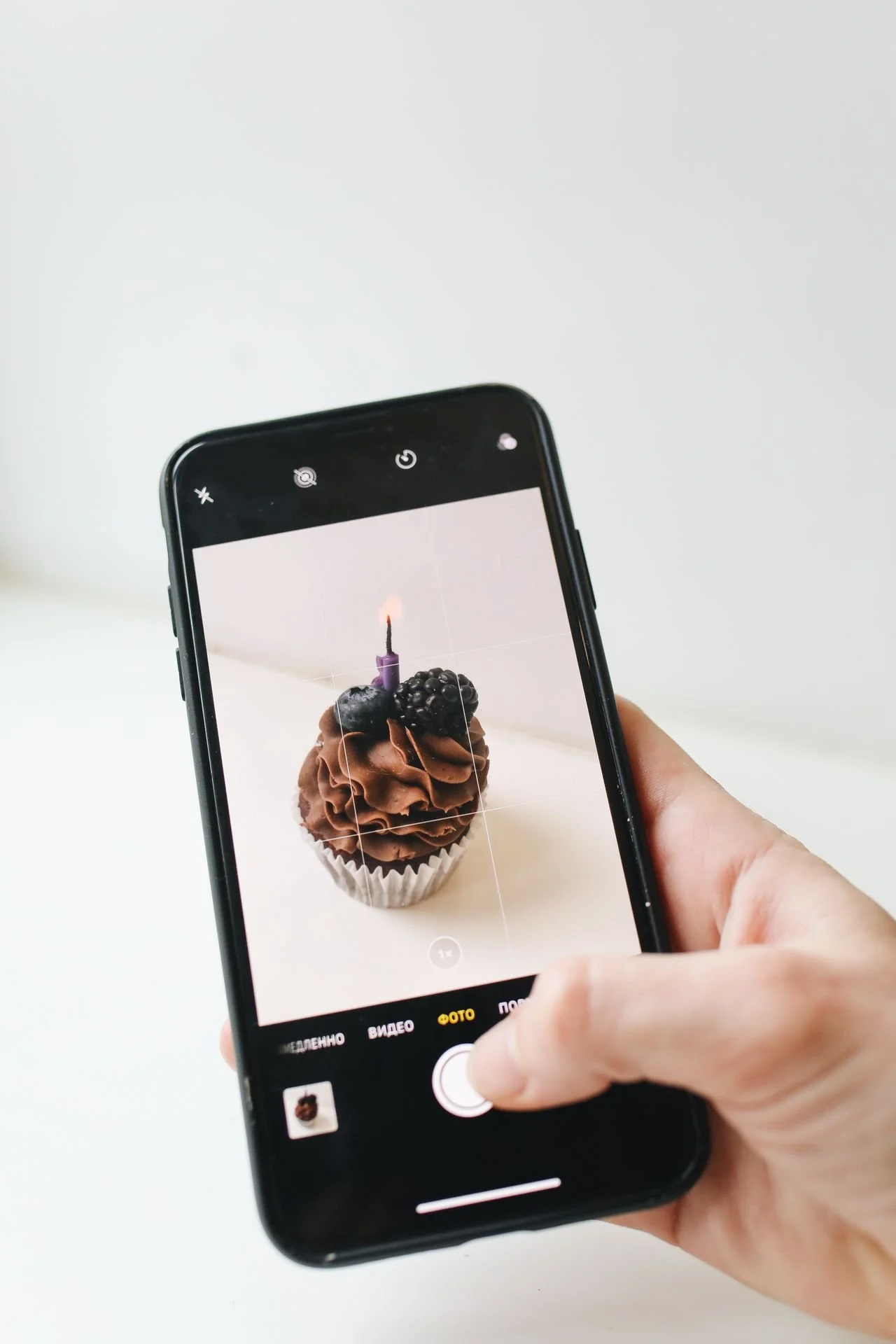 Phone screen shows camera app taking photo of a chocolate iced cupcake