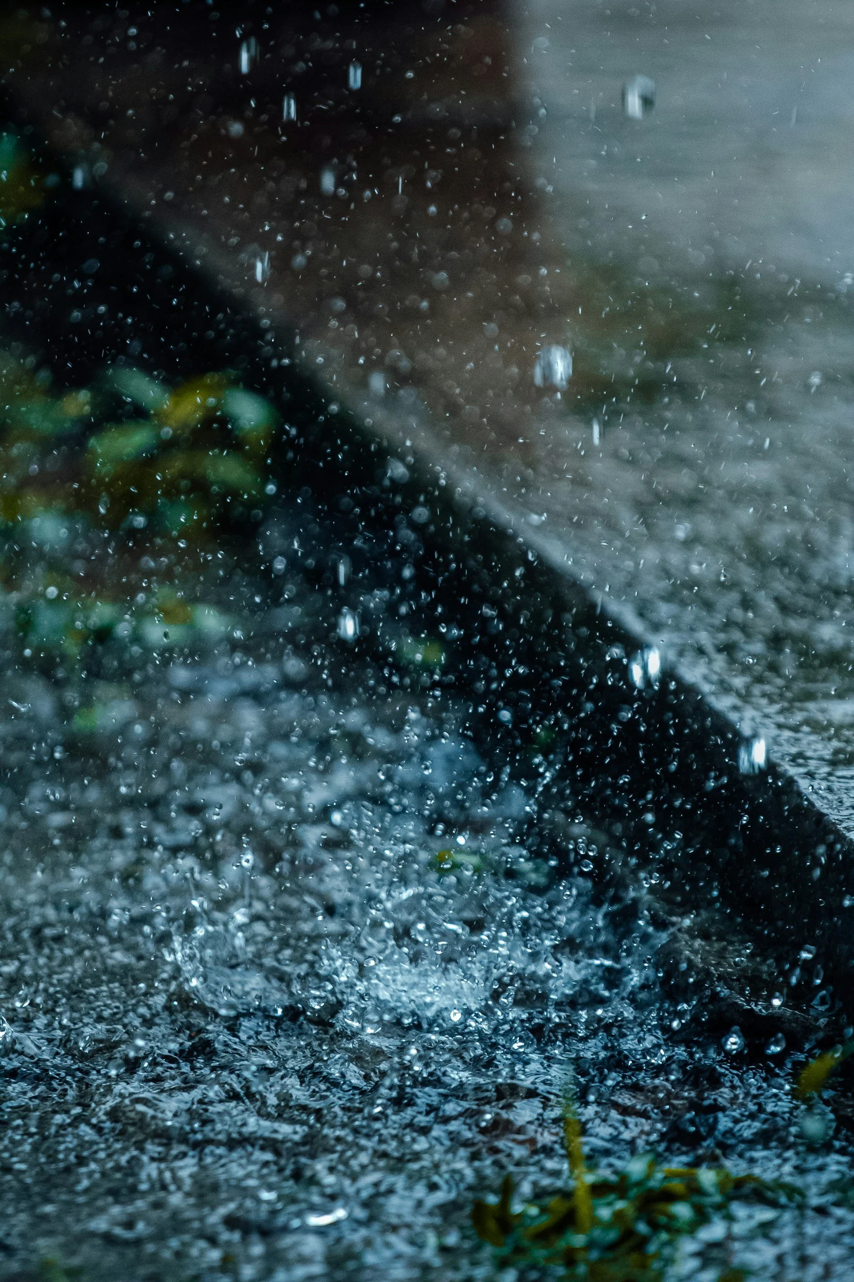 Rainy scene with water droplets splashing on the ground and a blurred background.