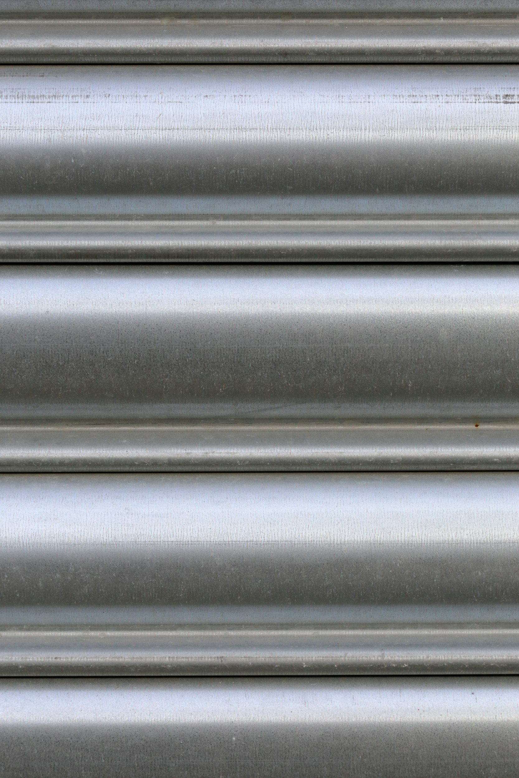 Close-up of metallic, silver, grooved surface, possibly a rolling shutter or metal siding.