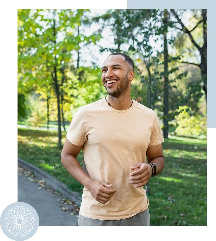 A smiling man jogging in a park on a sunny day, wearing a beige t-shirt and a smartwatch.