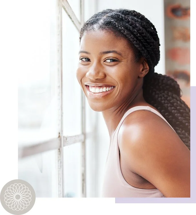A young woman with braided hair smiling and looking out of a window.