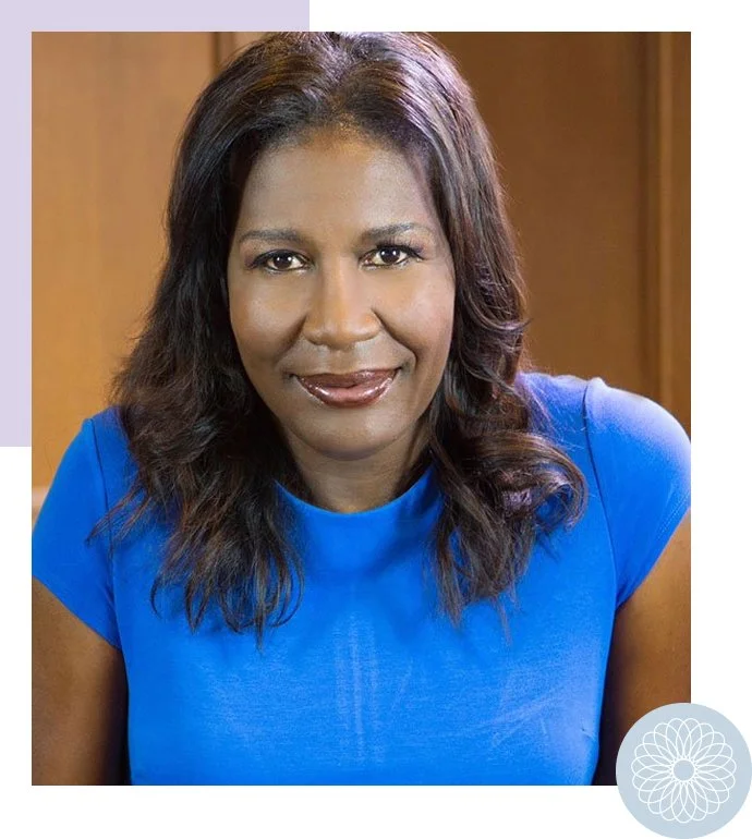 Portrait of a woman with dark hair in loose waves, wearing a bright blue top, smiling softly, with a wooden background.