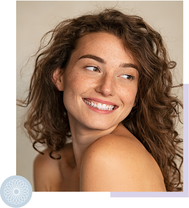 Close-up of a smiling woman with curly hair and freckles, looking away from the camera.