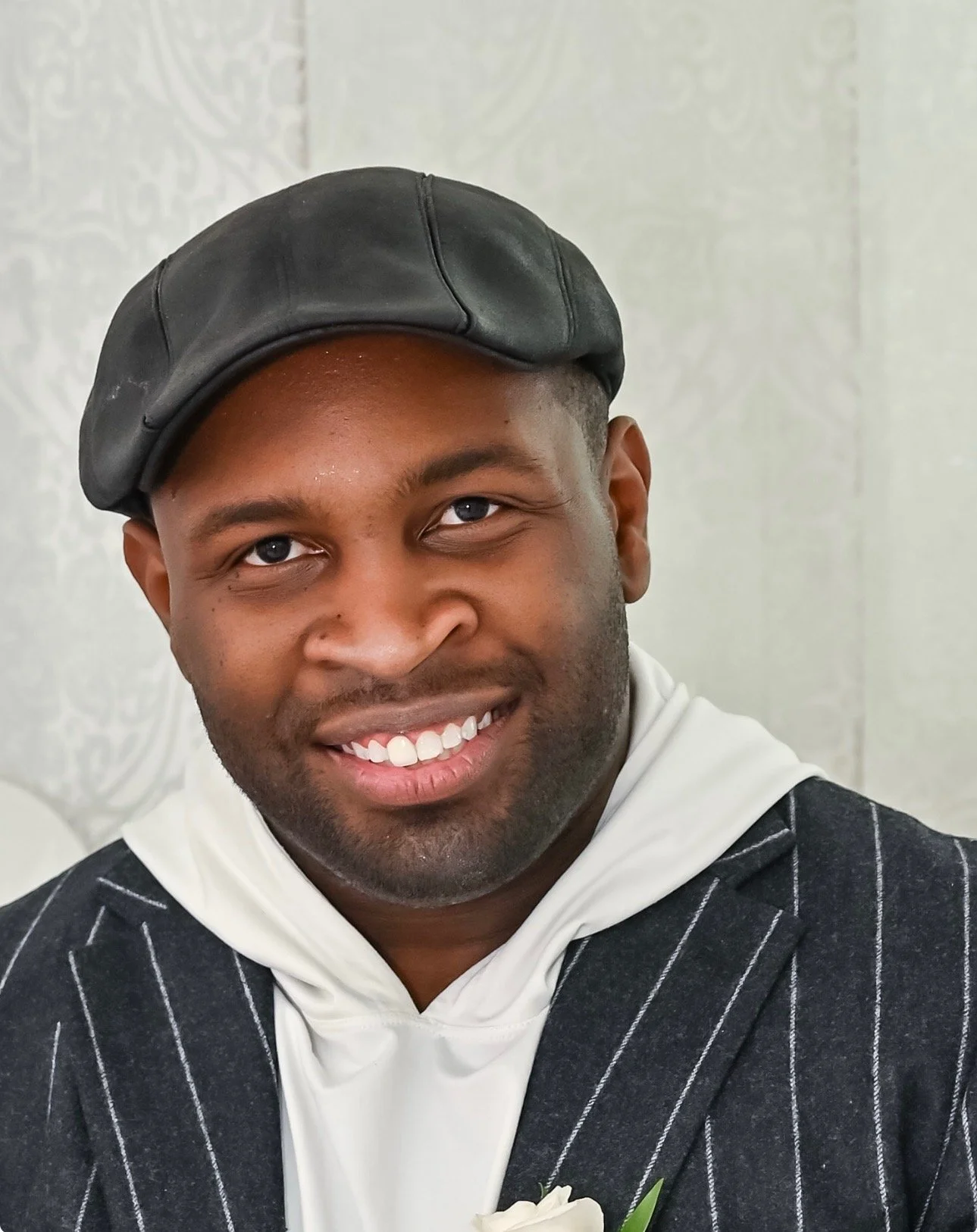 Smiling man in a pinstripe suit with a white shirt and a black leather cap.