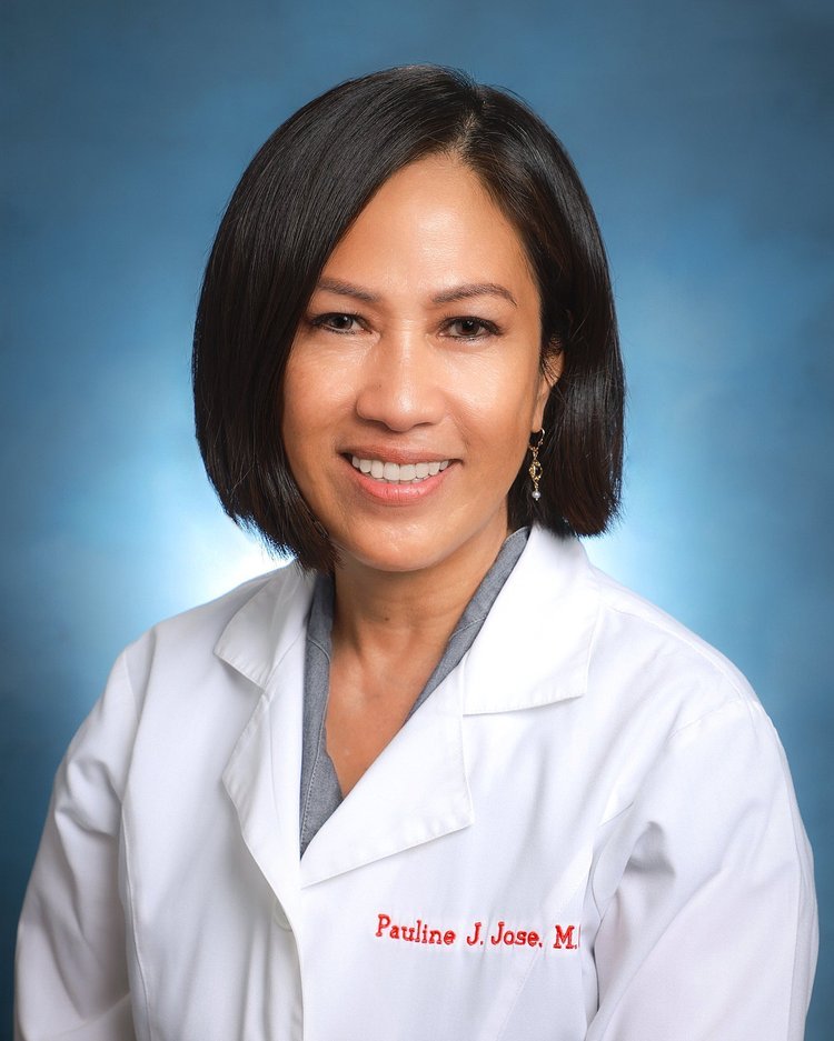 a woman with short black hair wearing a white medical coat with red embroidery that reads 'Pauline J. Jose, M.', smiling against a blue background.