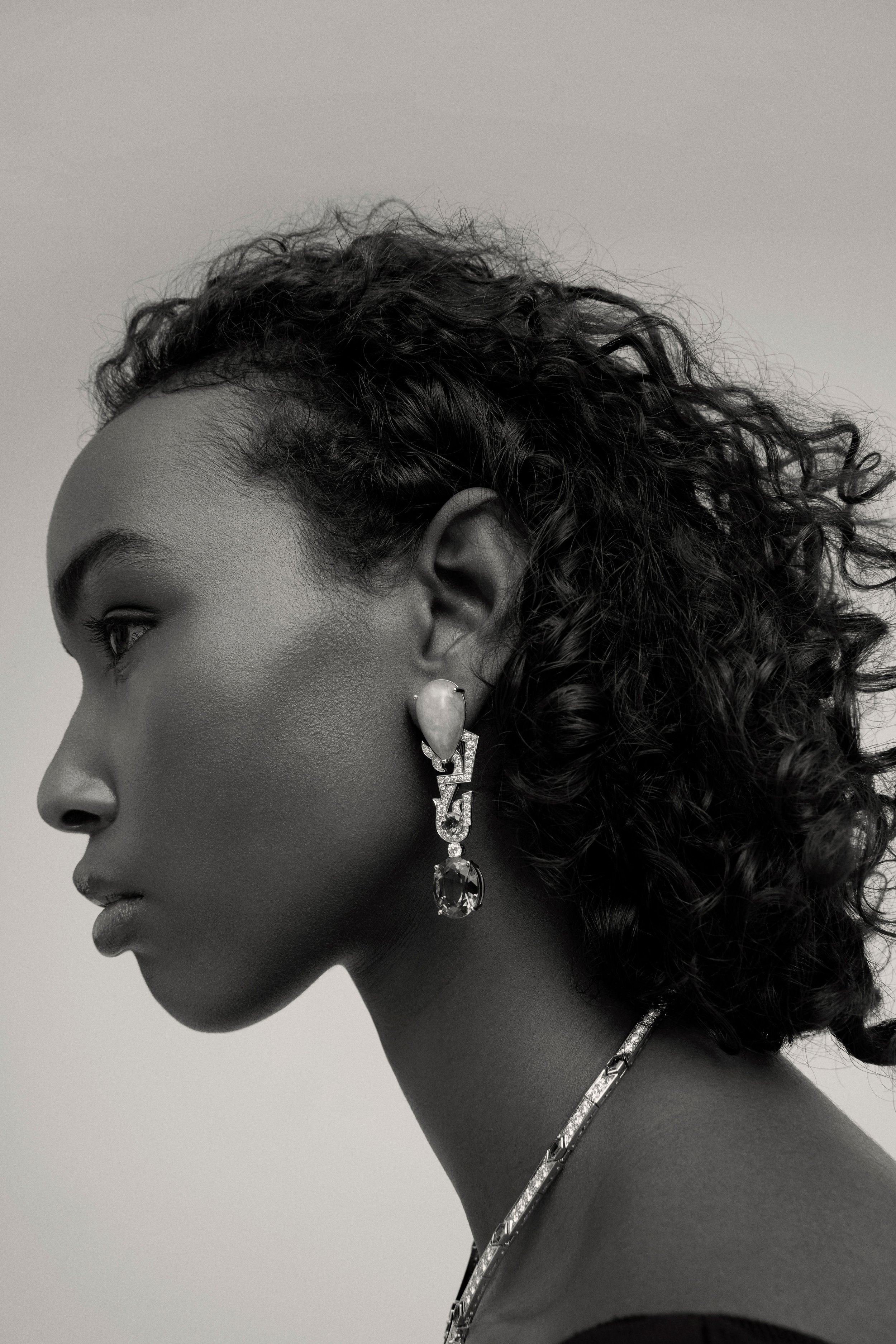 Portrait en noir et blanc d'une femme avec bouclettes courtes, portant une boucle d'oreille sophistiquée avec des pierres précieuses.
