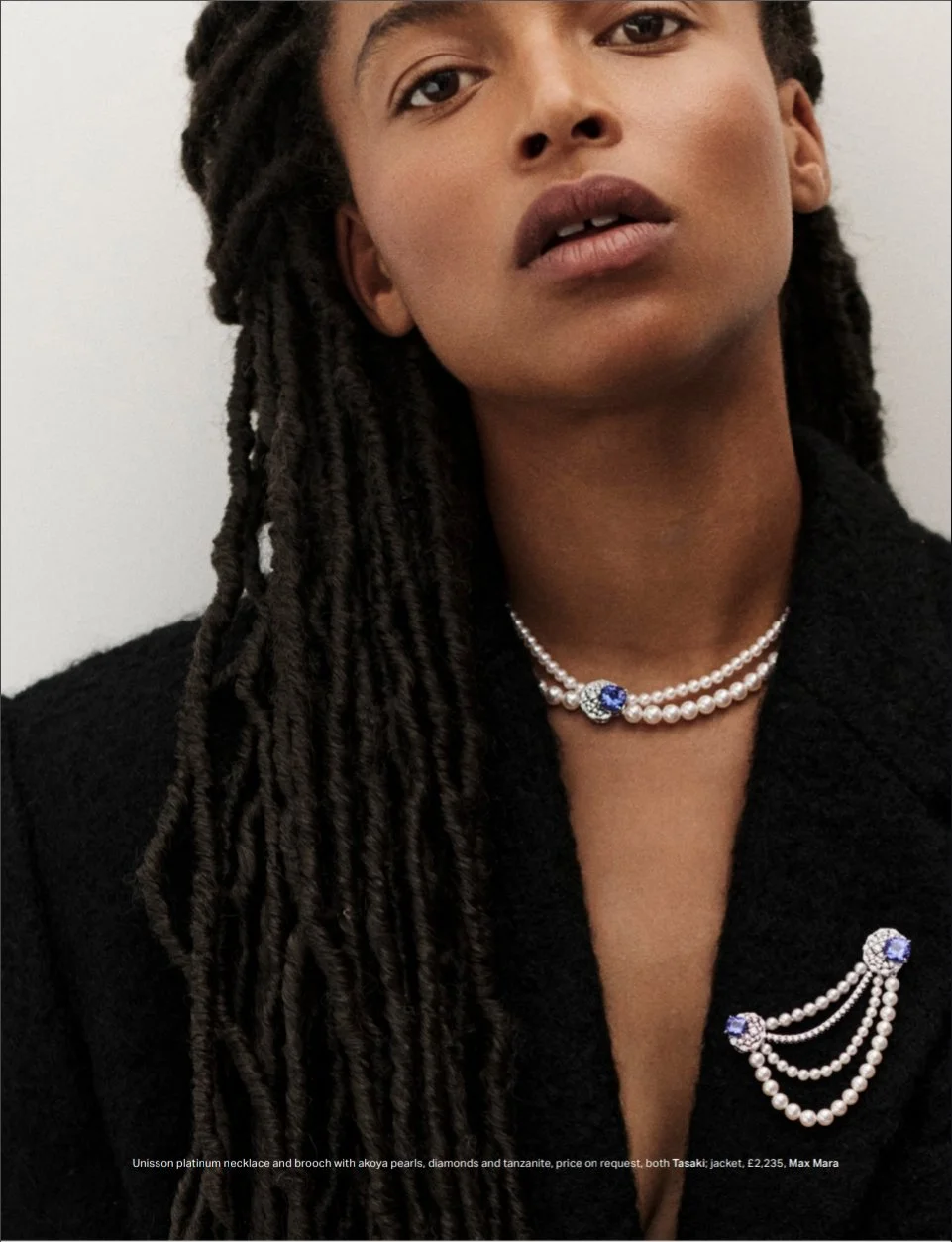 Portrait d'une femme portant des bijoux en perles, diamants, saphirs et tanzanite, avec une veste noire. La femme a de longues dreadlocks et un regard expressif.
