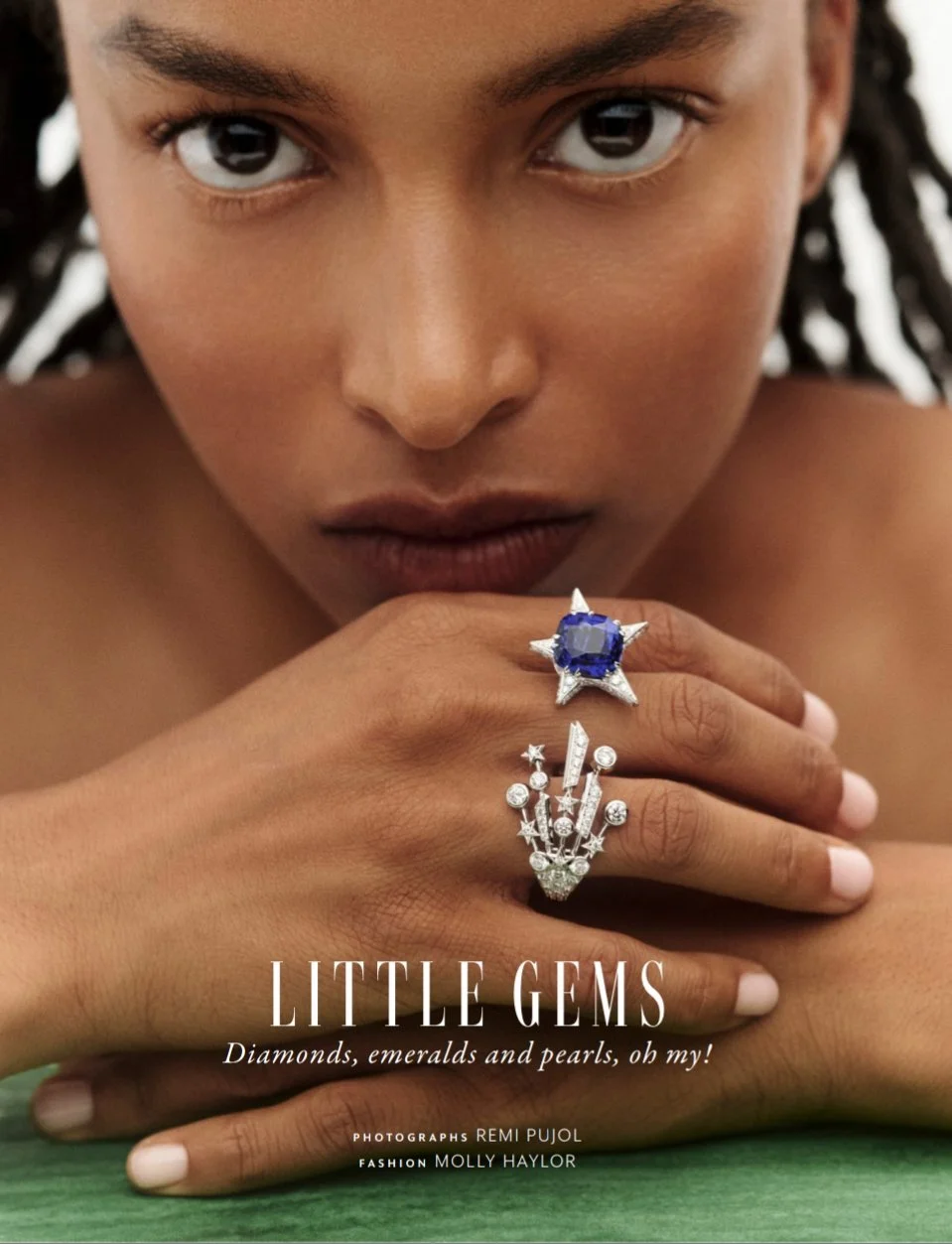 Une jeune femme avec des bijoux en main, portant une bague avec un grand saphir bleue entouré de diamants et une bague avec plusieurs diamants. Le texte mentionne des diamants, des émeraudes et des perles.