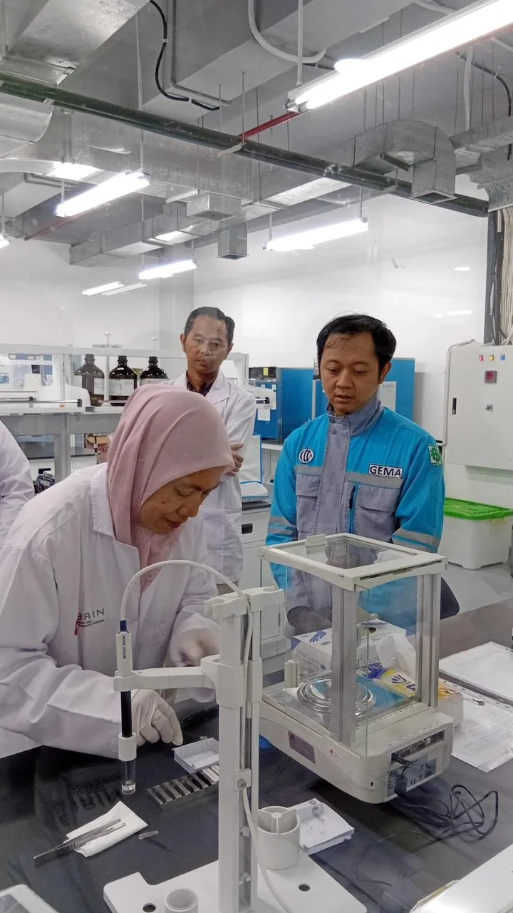 Scientists working in a laboratory, with one woman wearing a pink headscarf and white lab coat, analyzing samples, while three men observe the process.