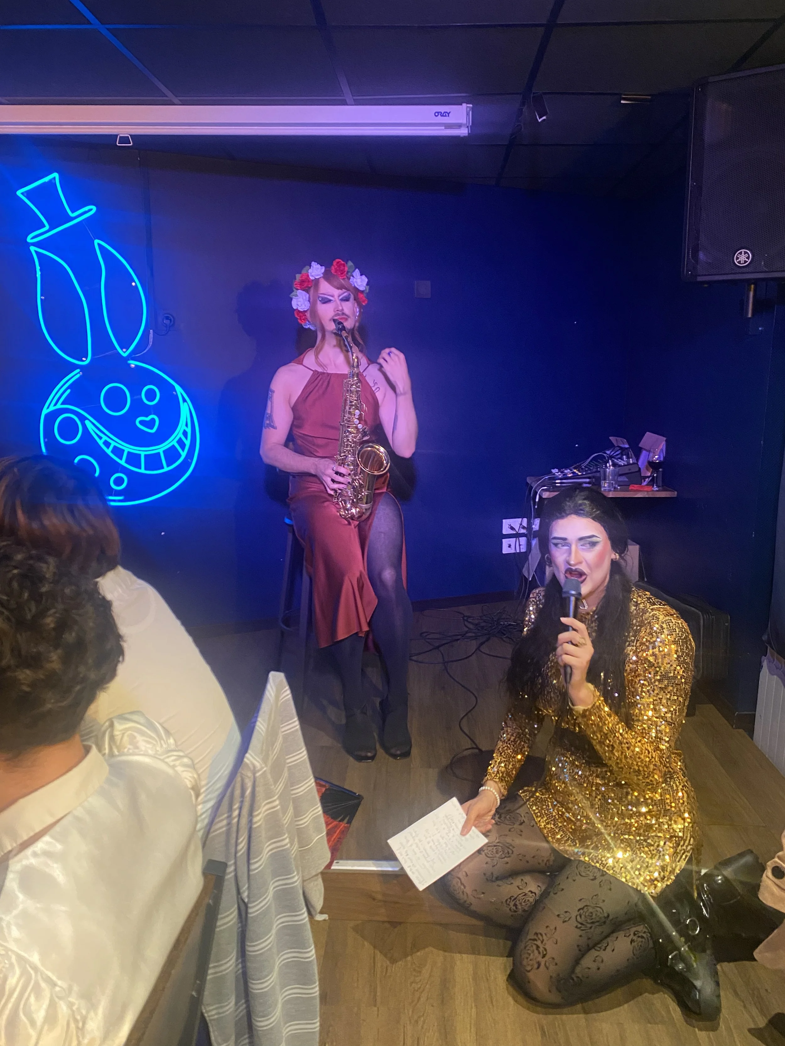 Une Drag Queen anime un blind test musical devant un public enthousiaste.