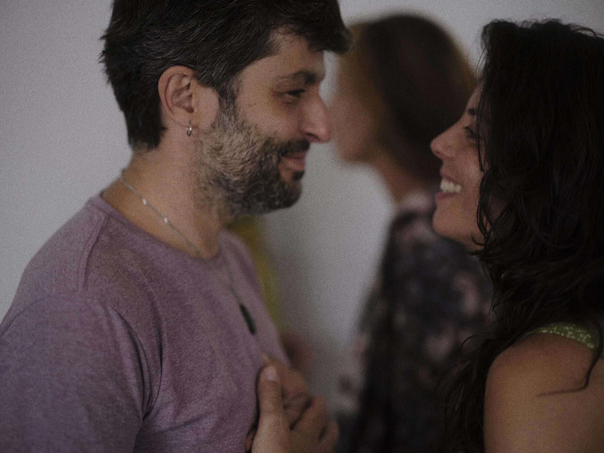 Un hombre y una mujer sonrientes y mirándose estrechamente en un momento romántico, con otra mujer difusa en el fondo