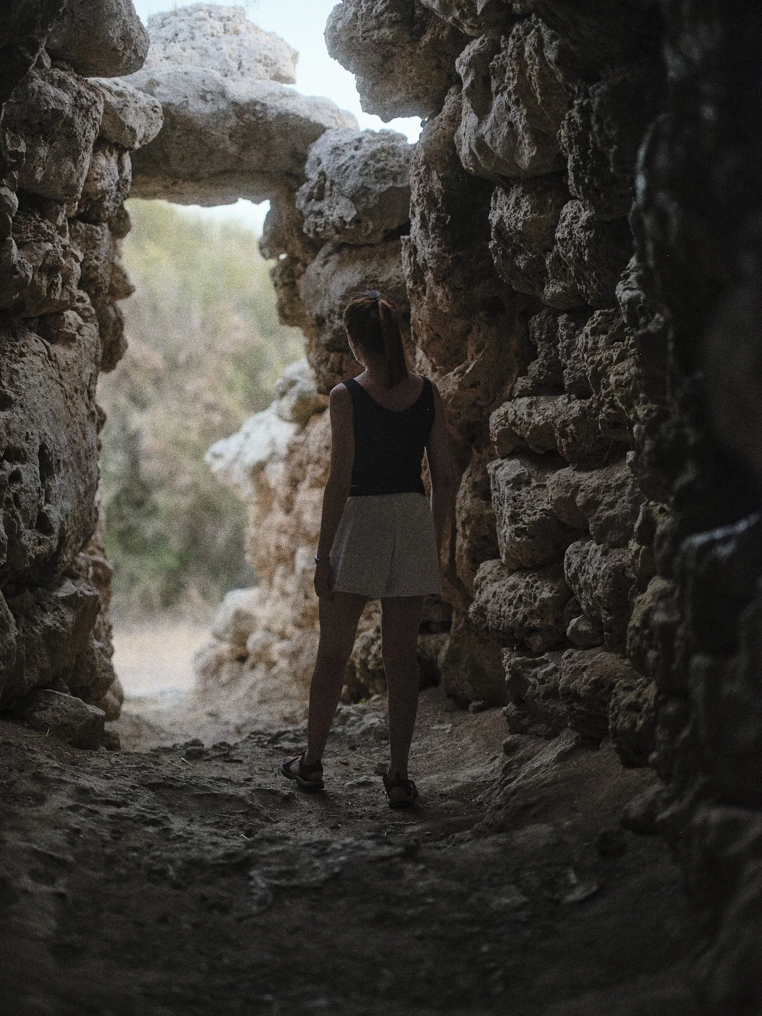 Mujer de espaldas en una cueva de piedras con luz natural al fondo.