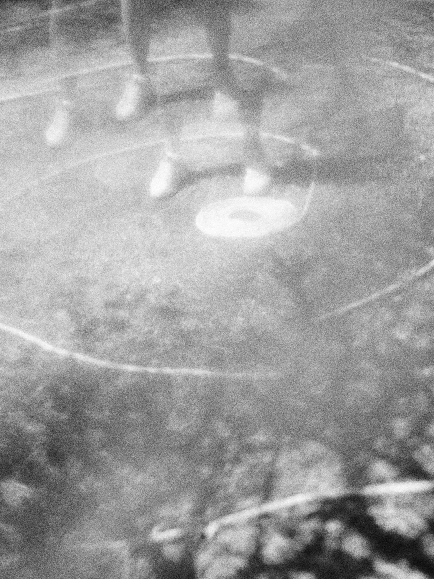 Una foto en blanco y negro de una persona caminando sobre una superficie plana, vista desde abajo, con las sombras de sus piernas y zapatos visibles.