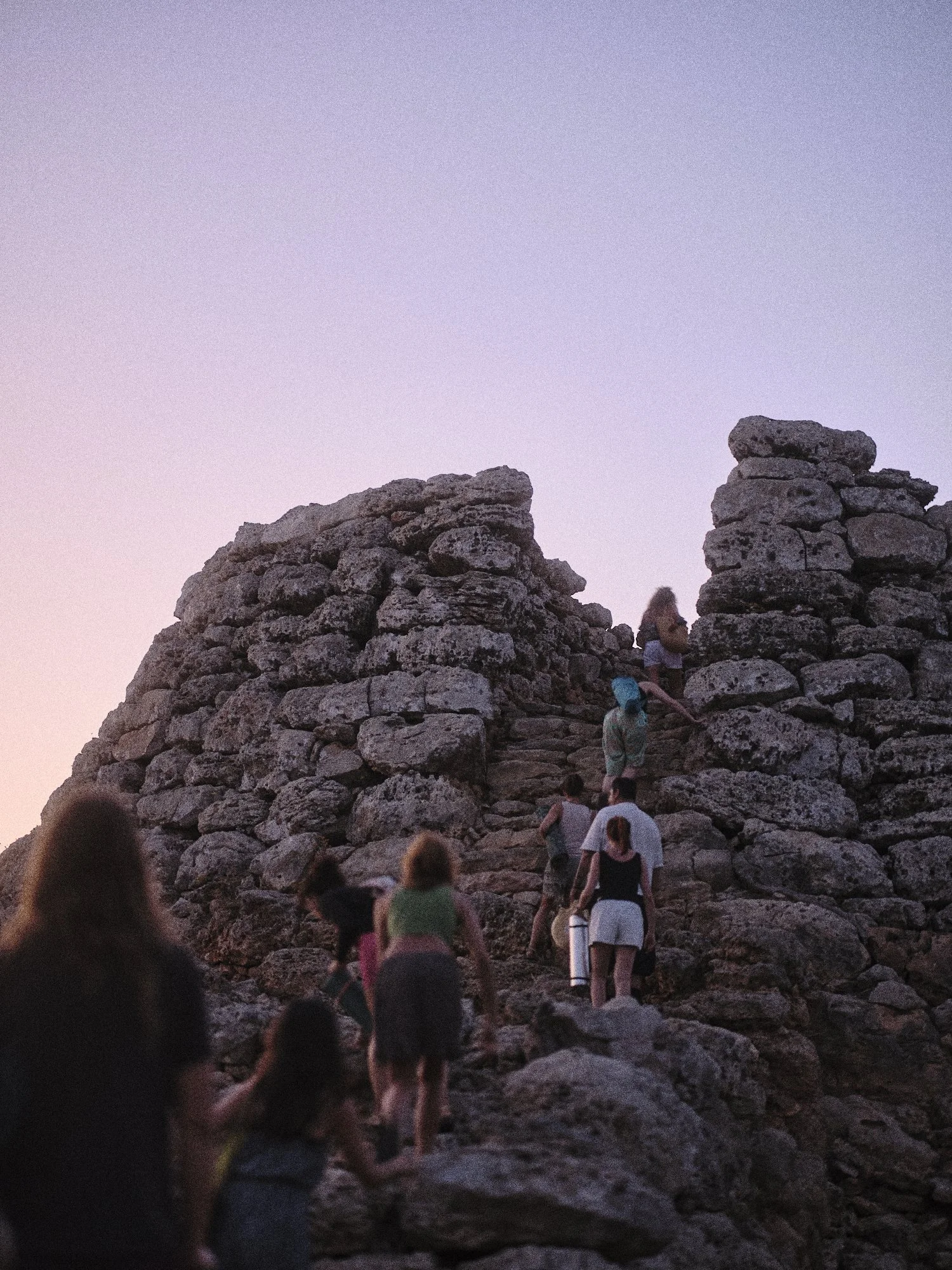 Grupo de personas ascendiendo por una estructura de piedras en un entorno natural al atardecer.
