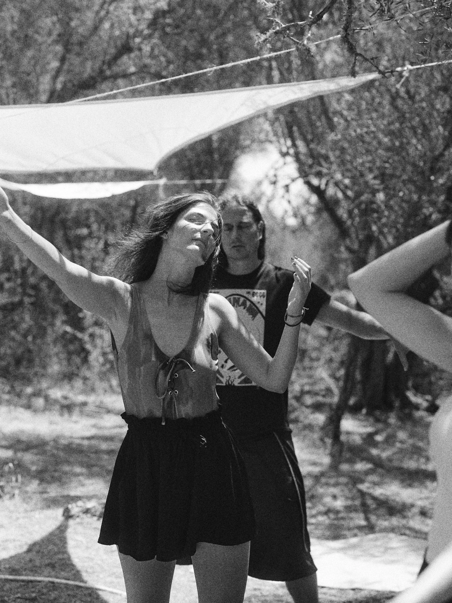 Jóvenes en un parque con sombra de árboles, disfrutando del día, en un momento capturado en una foto en blanco y negro.