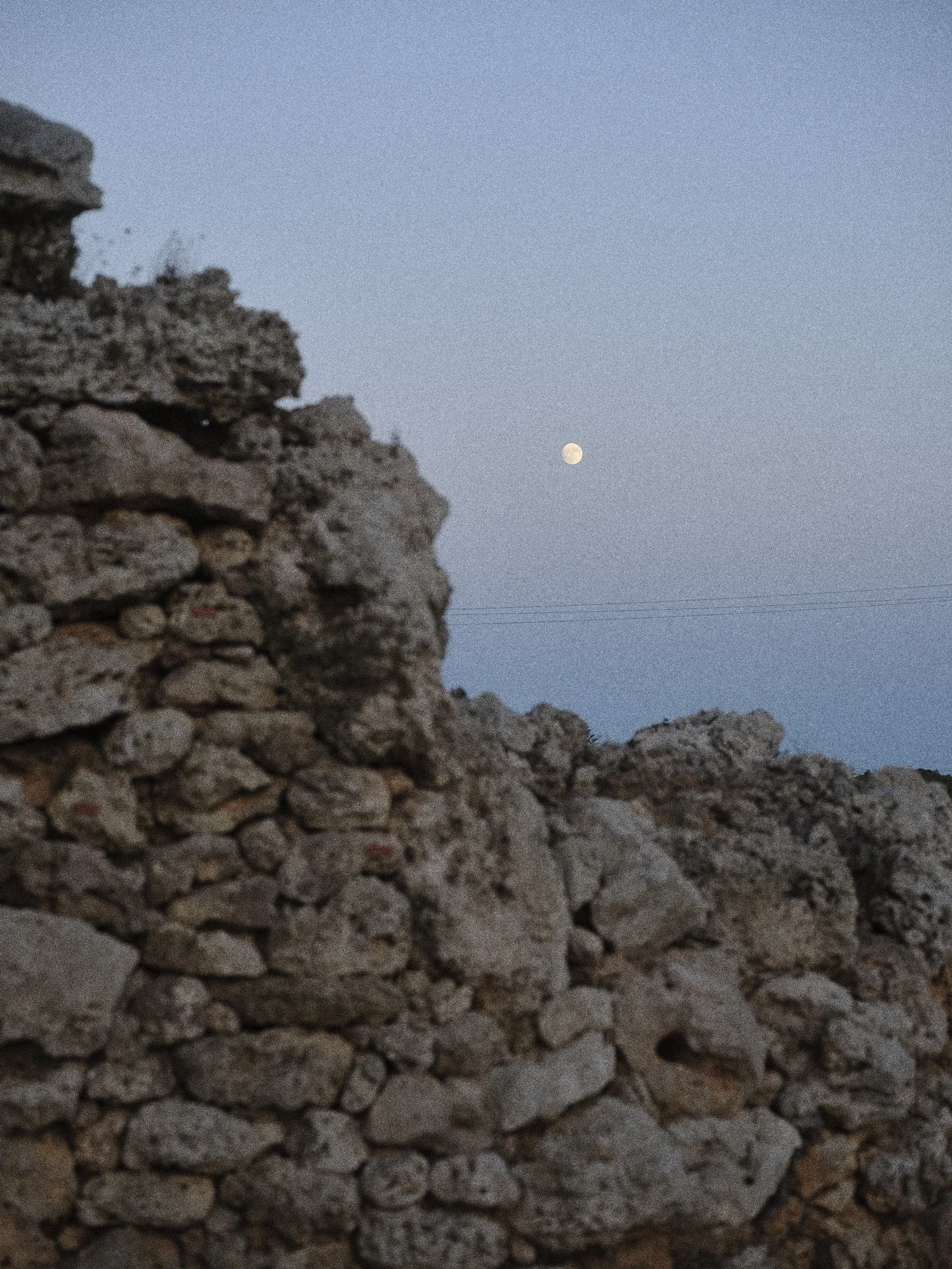 Montón de rocas, con la luna visible en el cielo crepuscular.