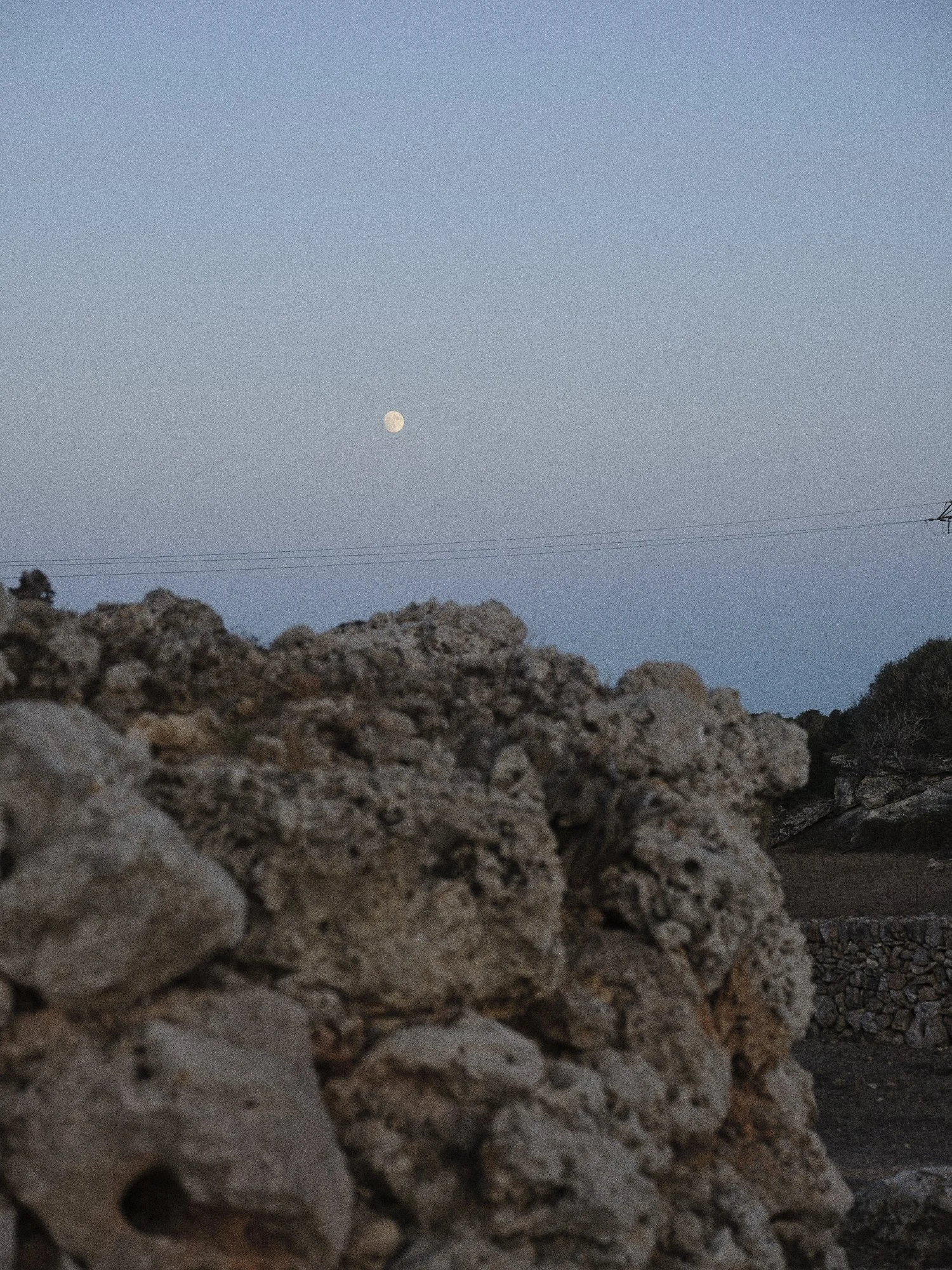 Puente de piedra en primer plano con el cielo azul y la luna visible en el fondo.